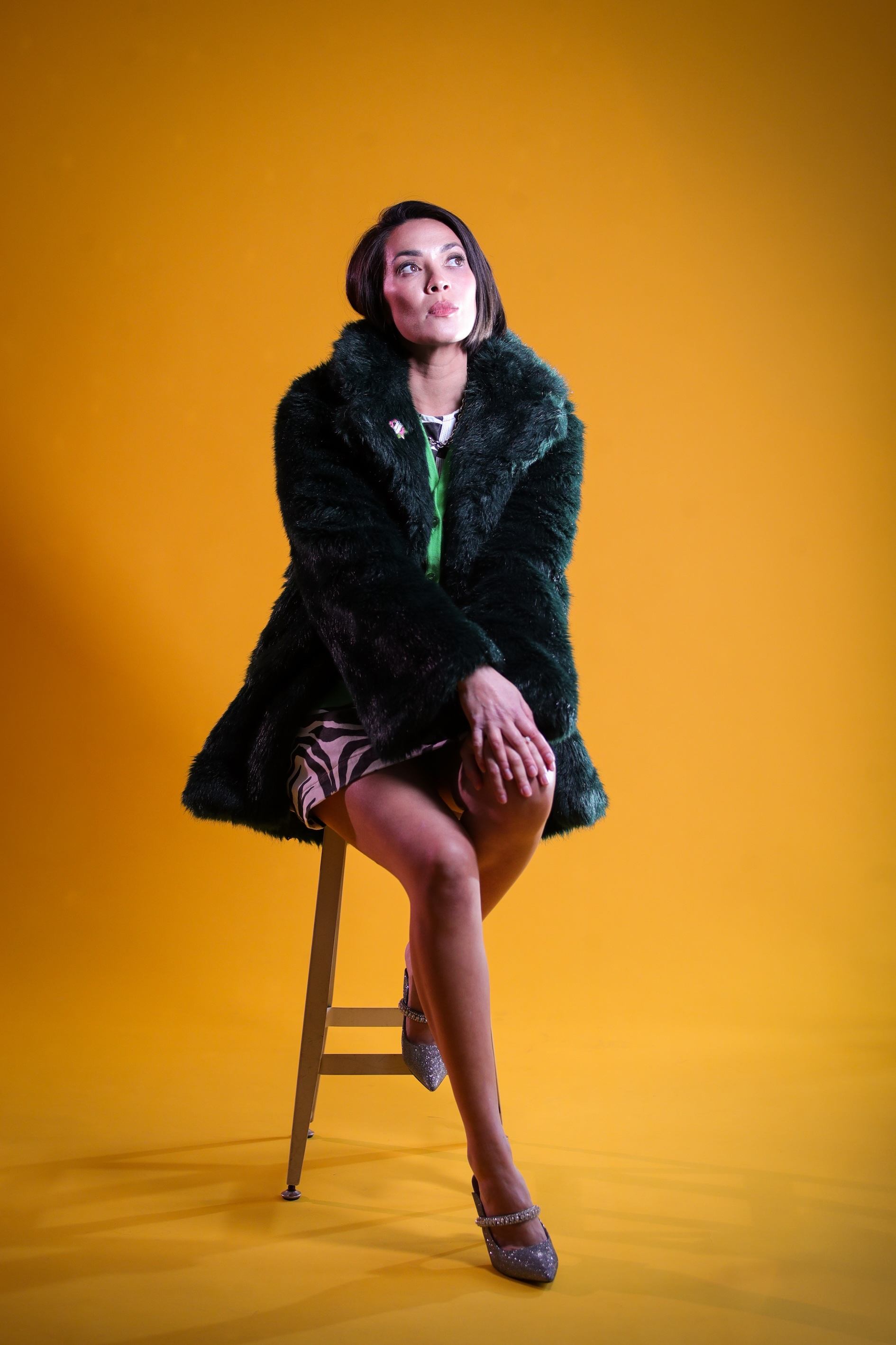 a woman in a green fur coat sitting on a stool