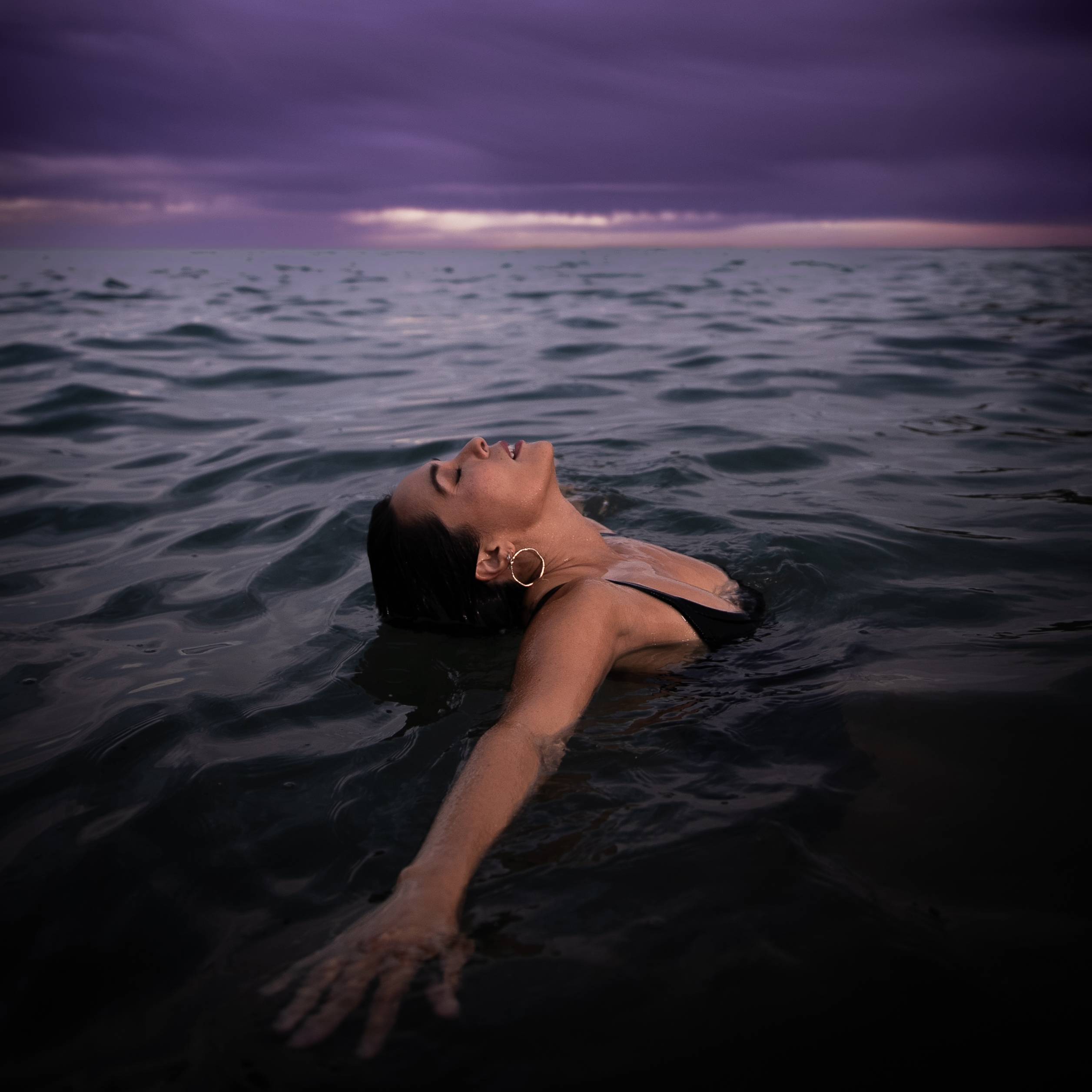 a woman floating in the ocean under a purple sky