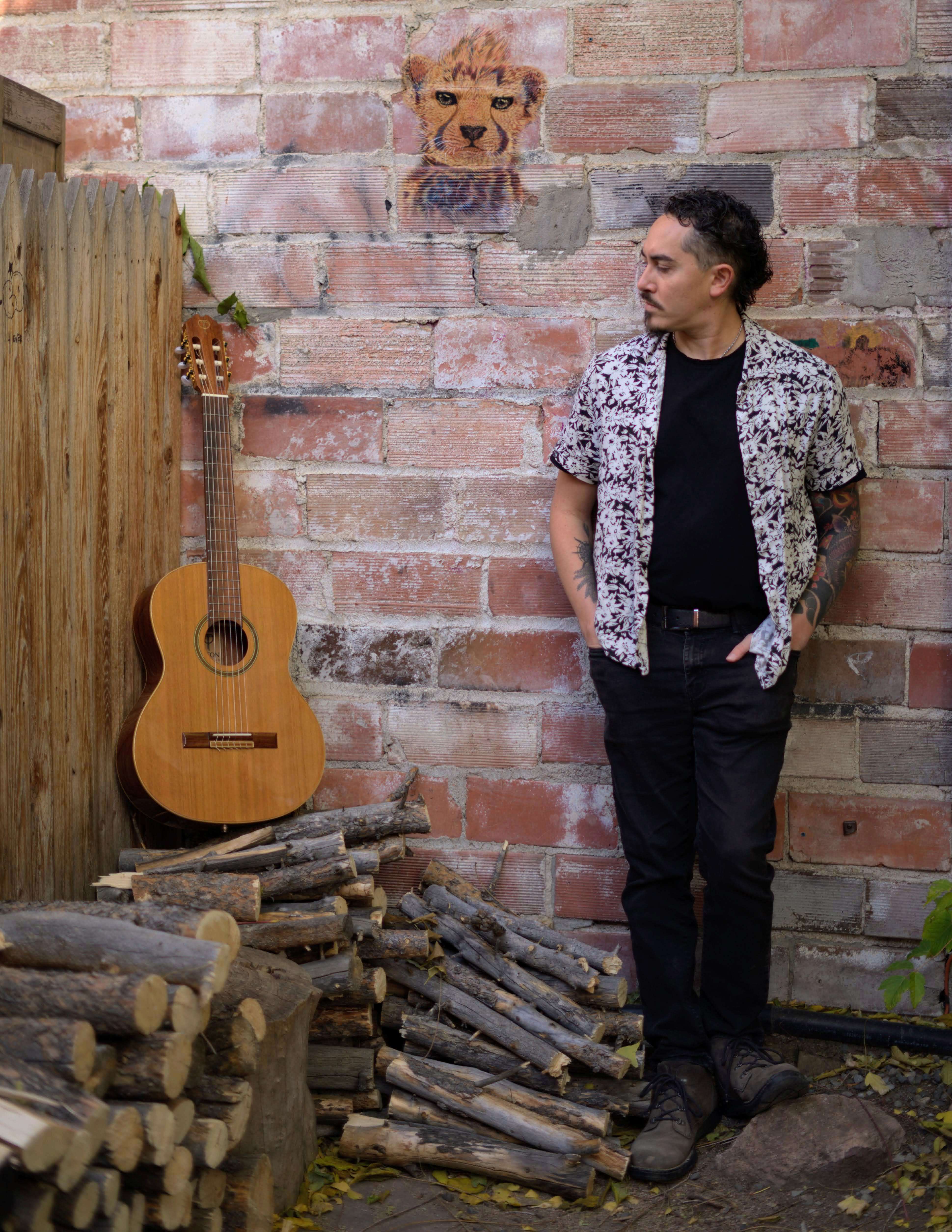a man leaning against a brick wall with an acoustic guitar