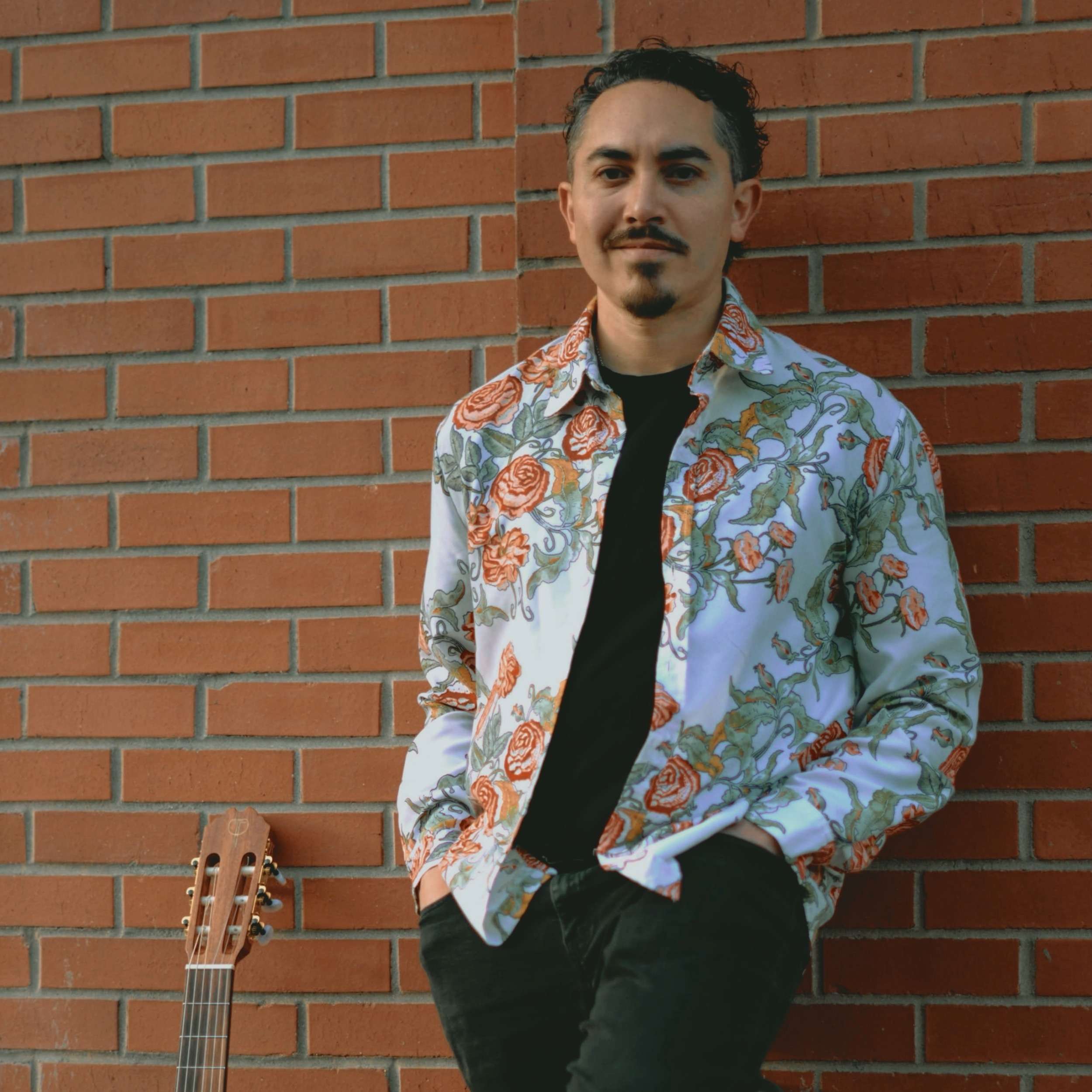 a man leaning against a brick wall with an acoustic guitar