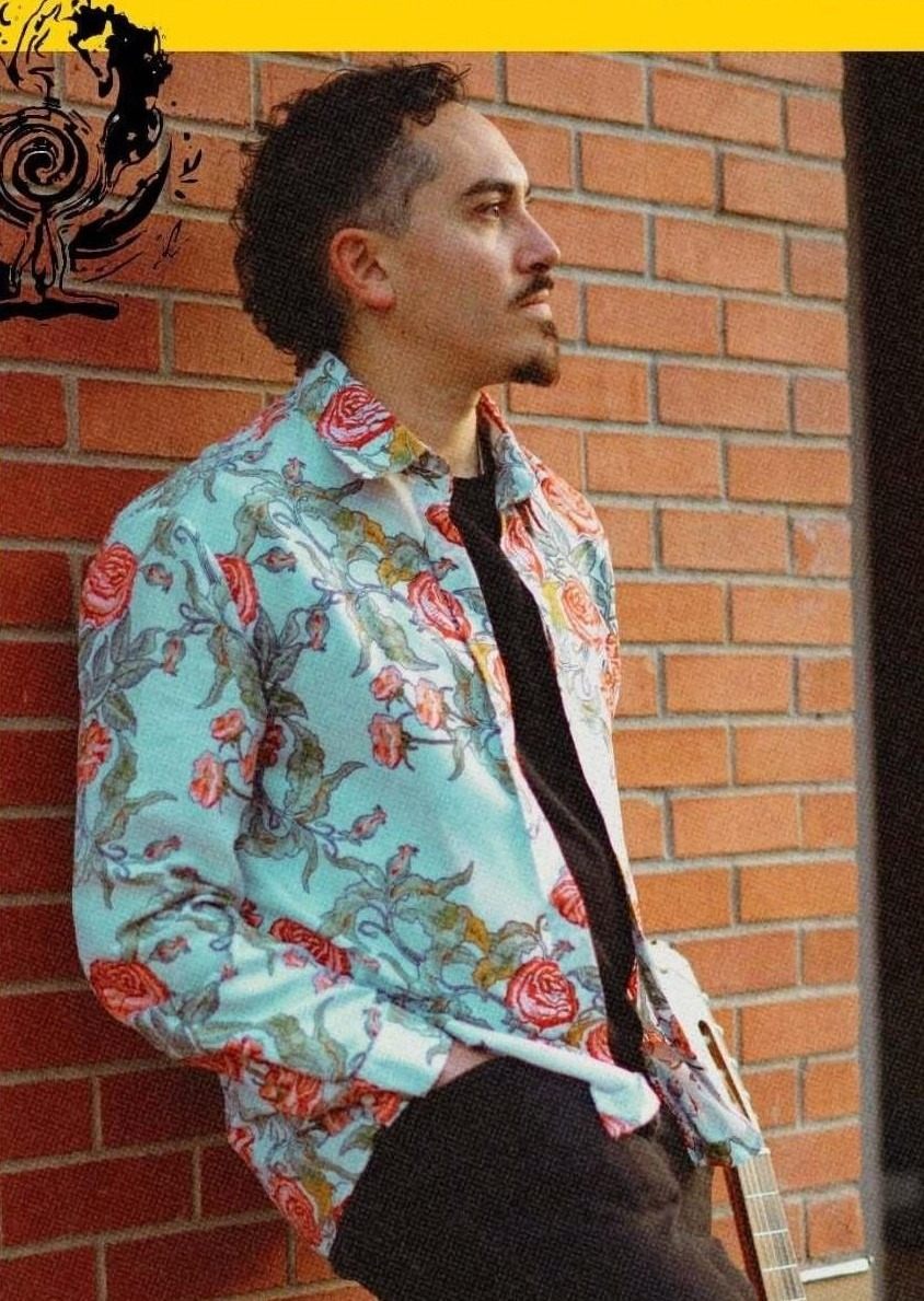 a man in a floral shirt leaning against a brick wall