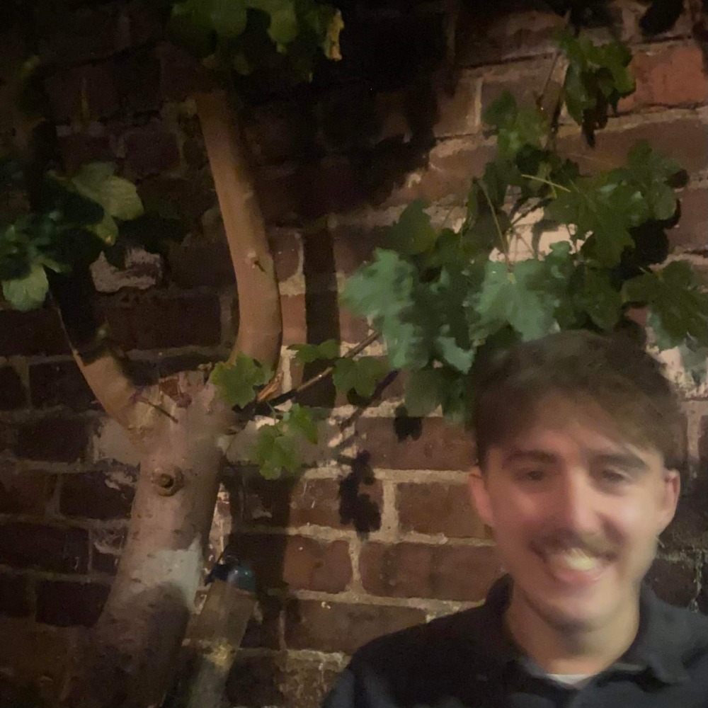 a man is smiling in front of a brick wall