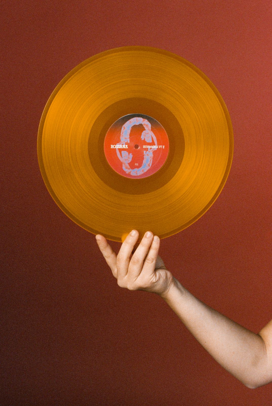 a woman holding an orange vinyl record on a red background