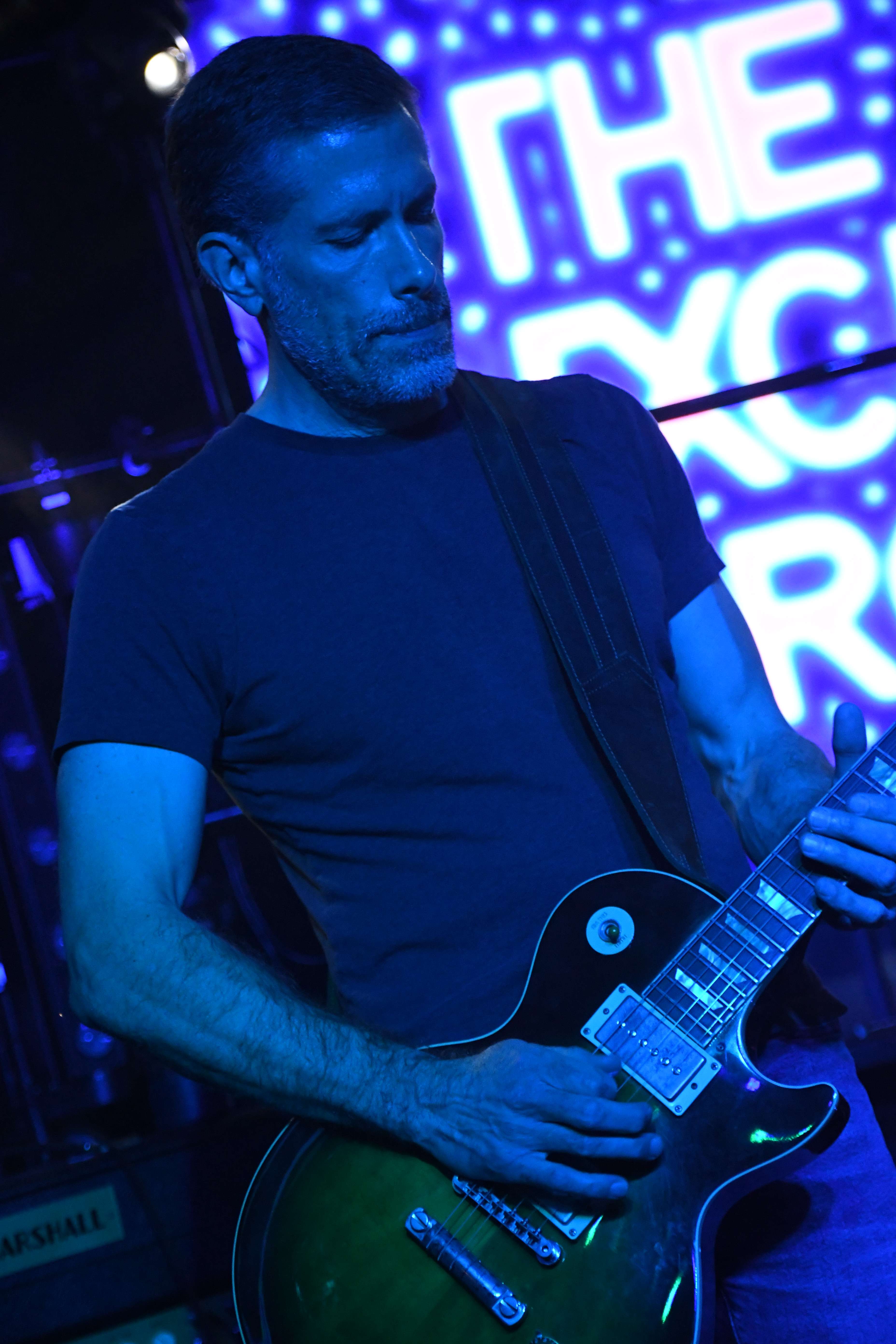 a man playing a guitar in front of a neon sign