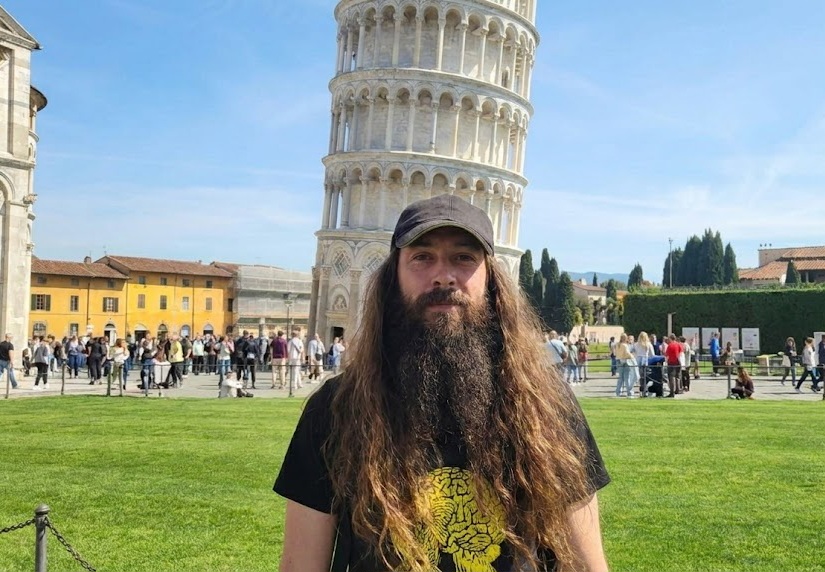 a bearded man standing in front of the leaning tower of pisa