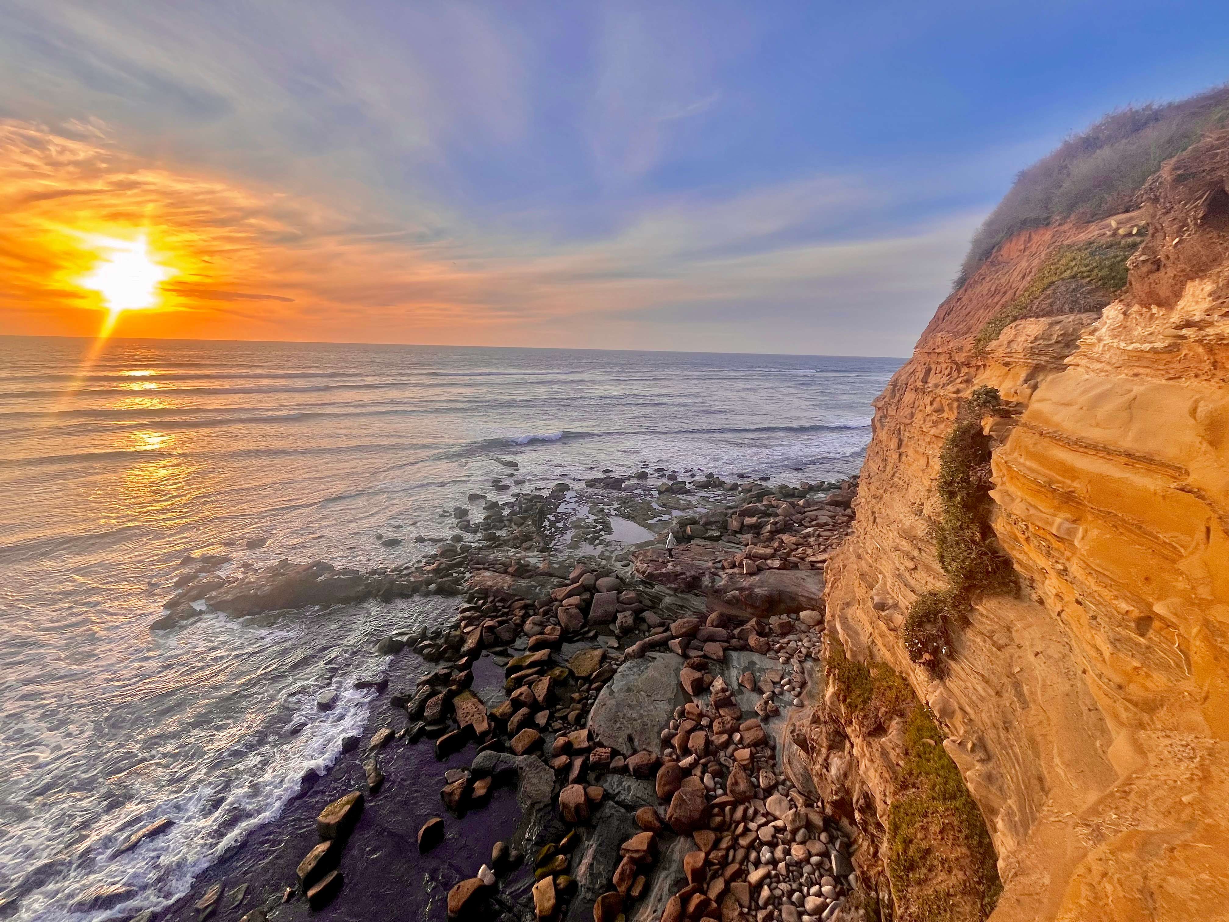 the sun is setting over the ocean and cliffs