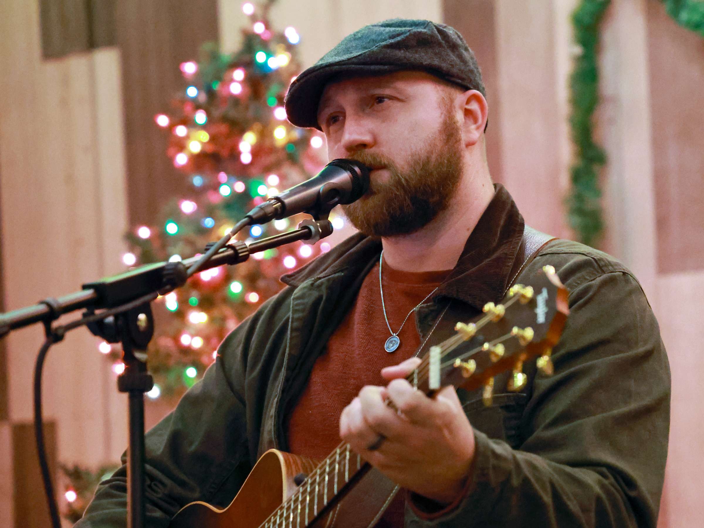 a bearded man playing an acoustic guitar in front of a christmas tree