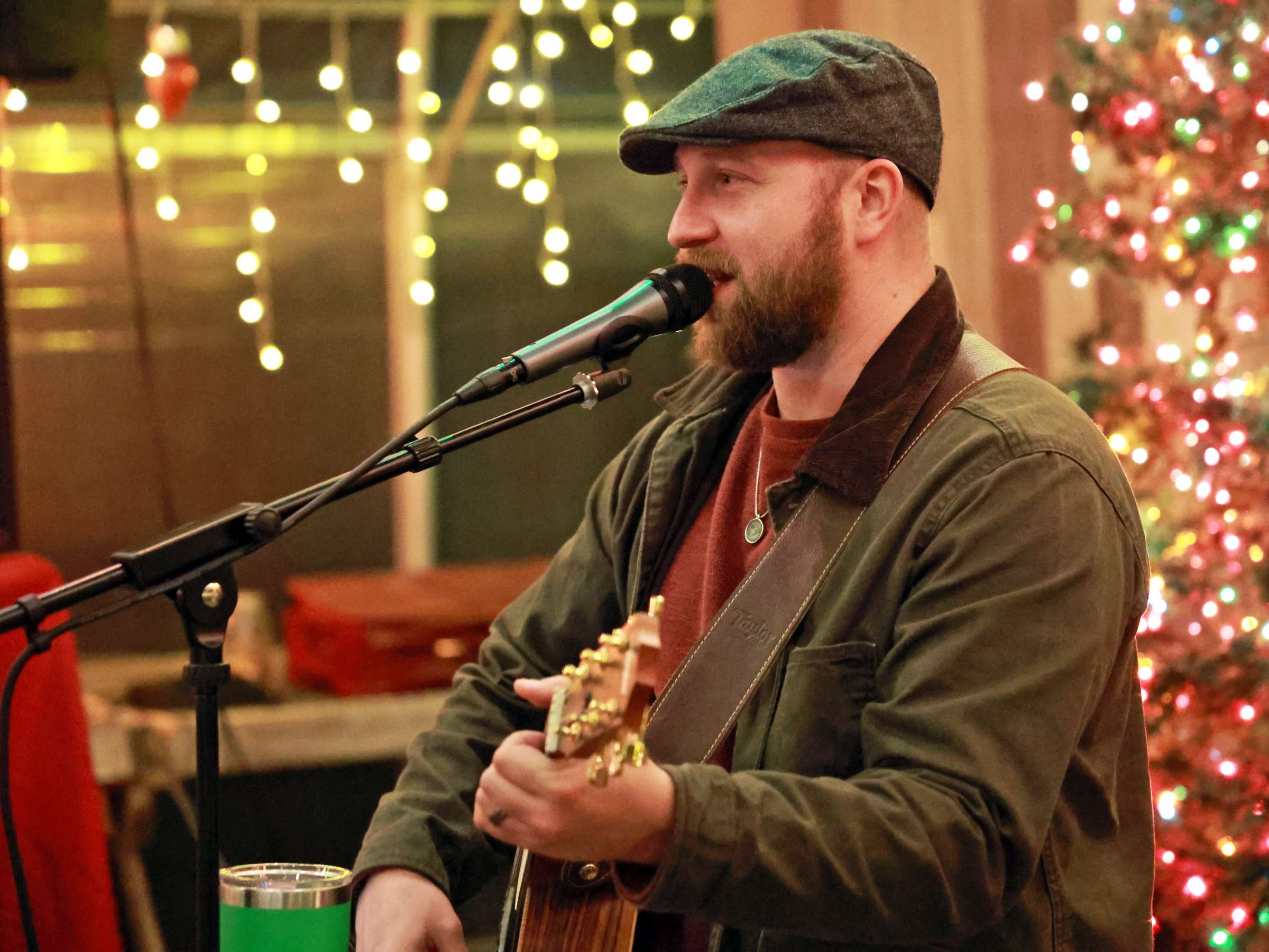 a bearded man playing an acoustic guitar in front of a christmas tree