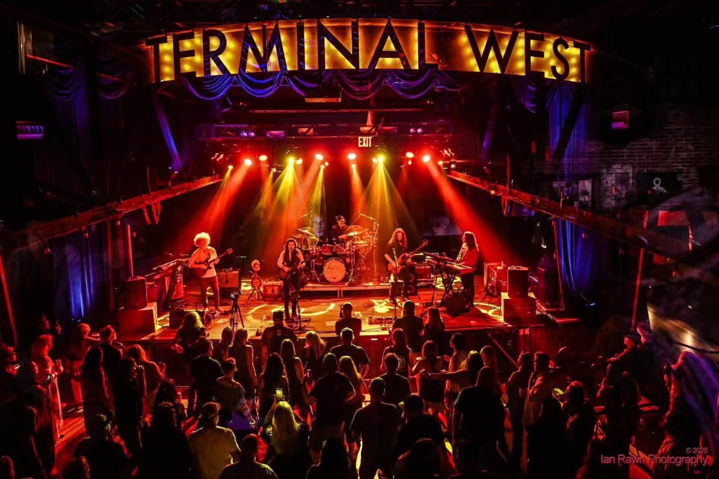 a group of people standing in front of a stage with the words terminal west