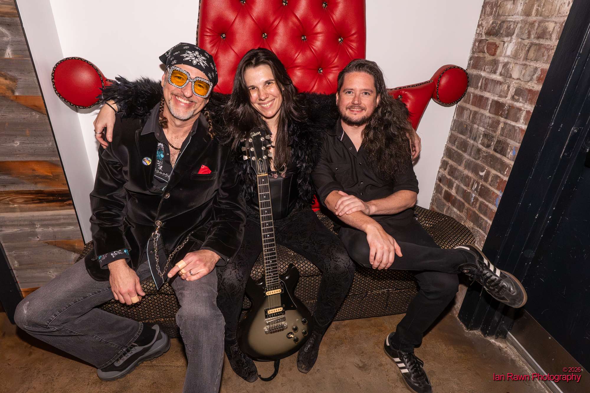 three people posing with guitars in front of a red couch