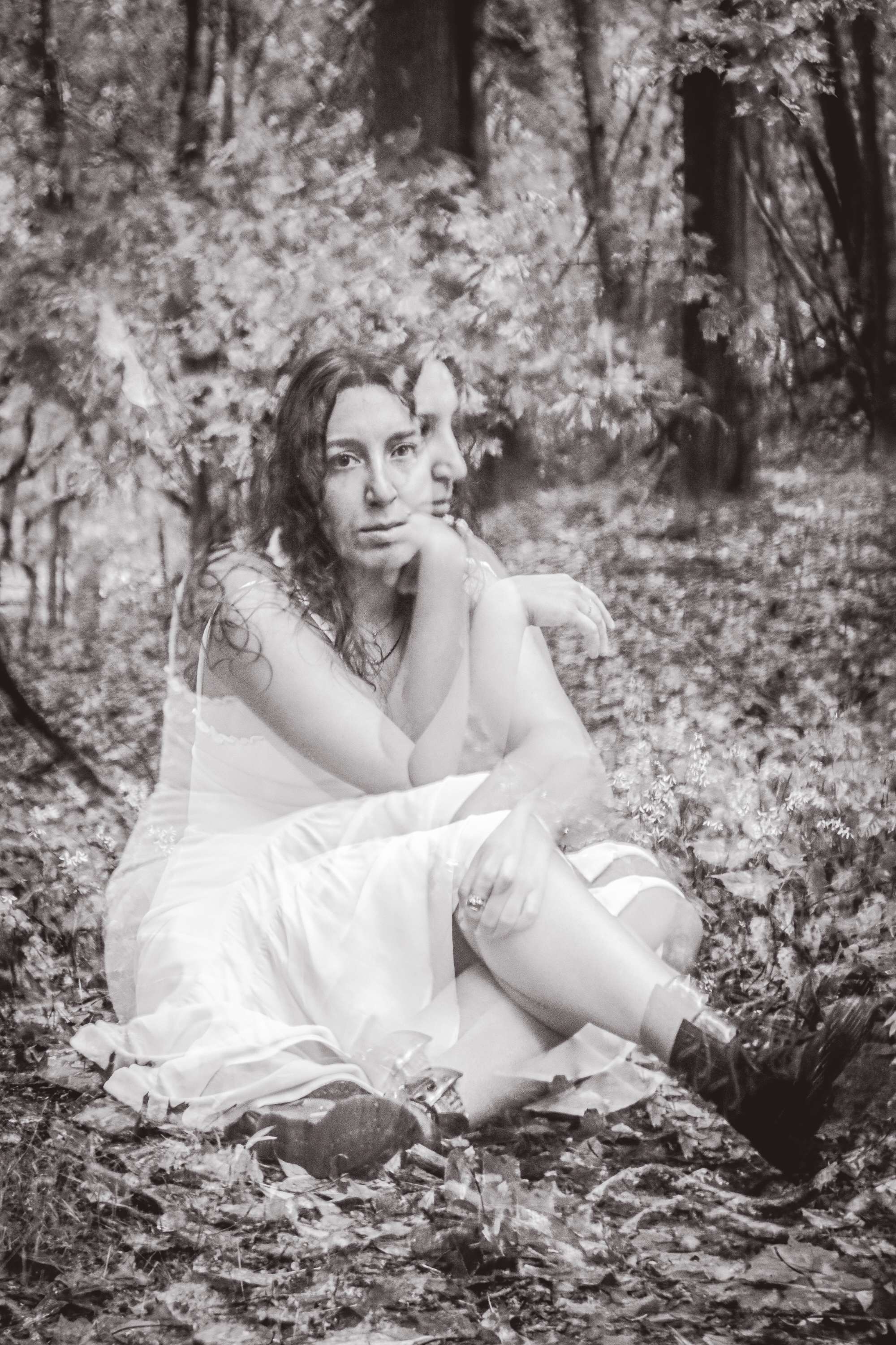 a black and white photo of a woman sitting in the woods