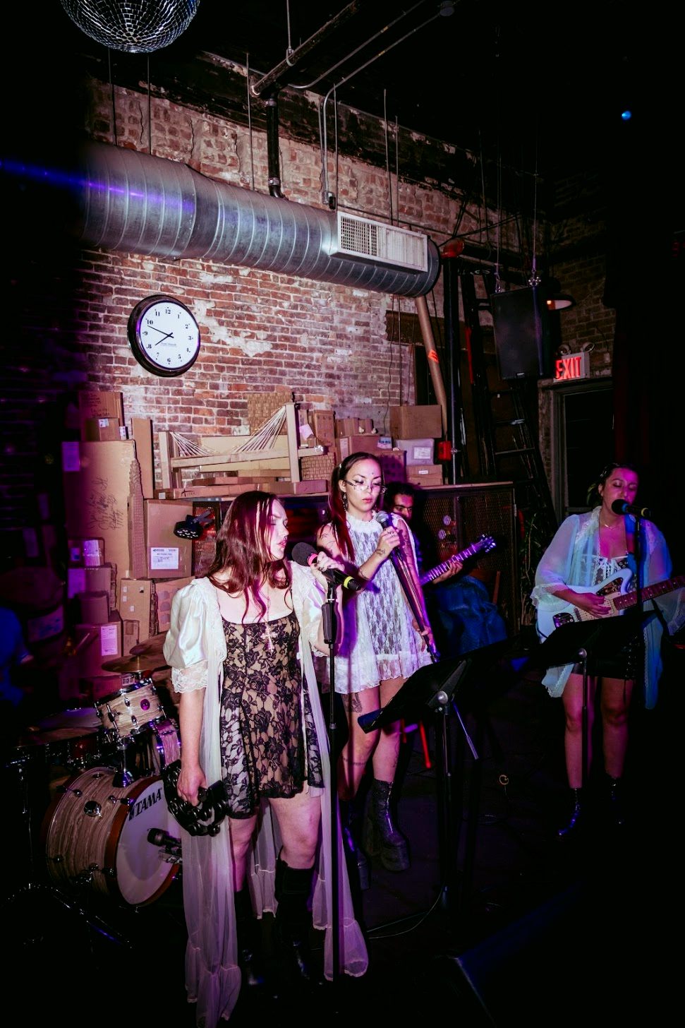 a group of women singing on stage in front of a brick wall