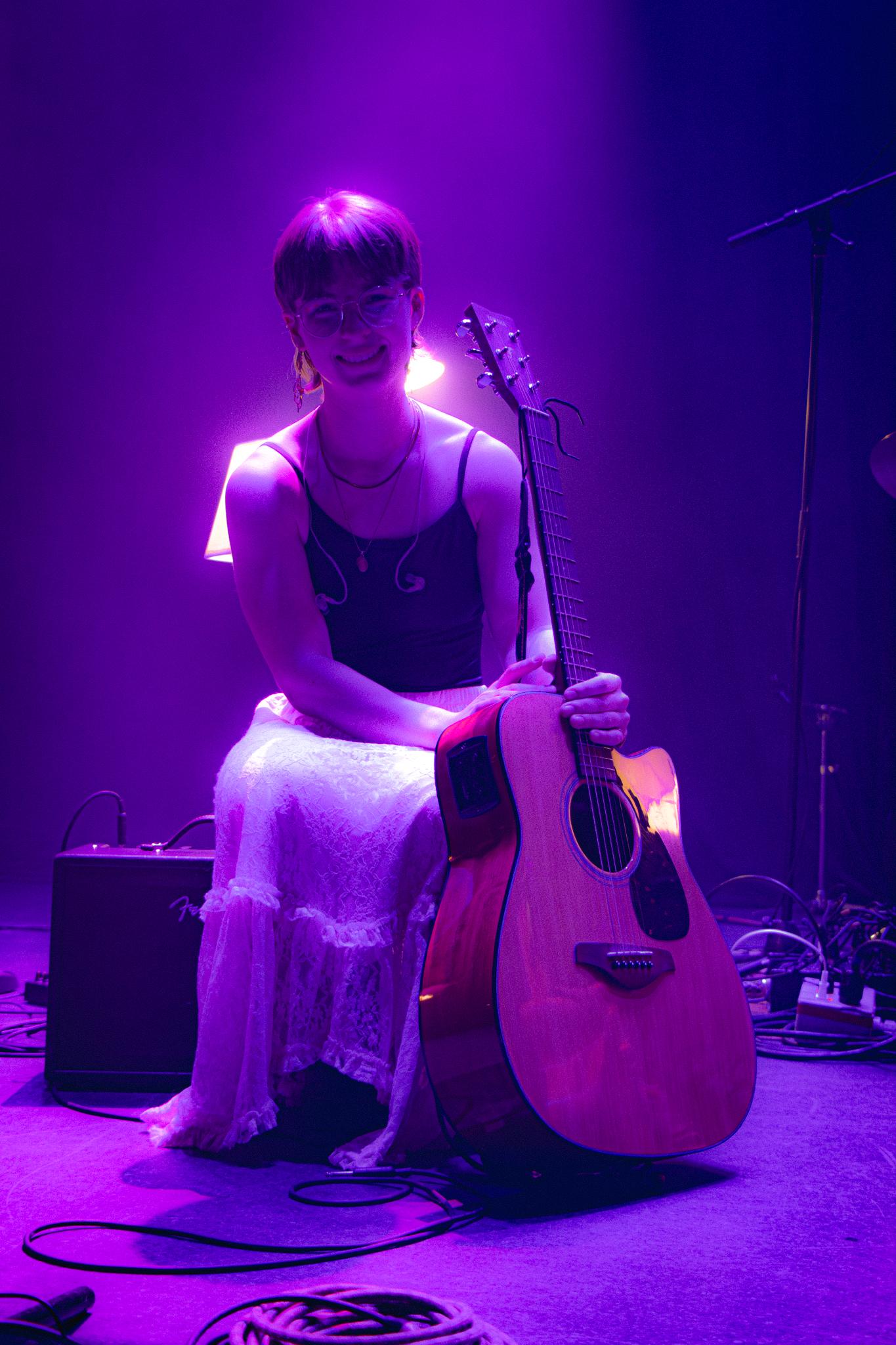 a woman sitting on stage with an acoustic guitar