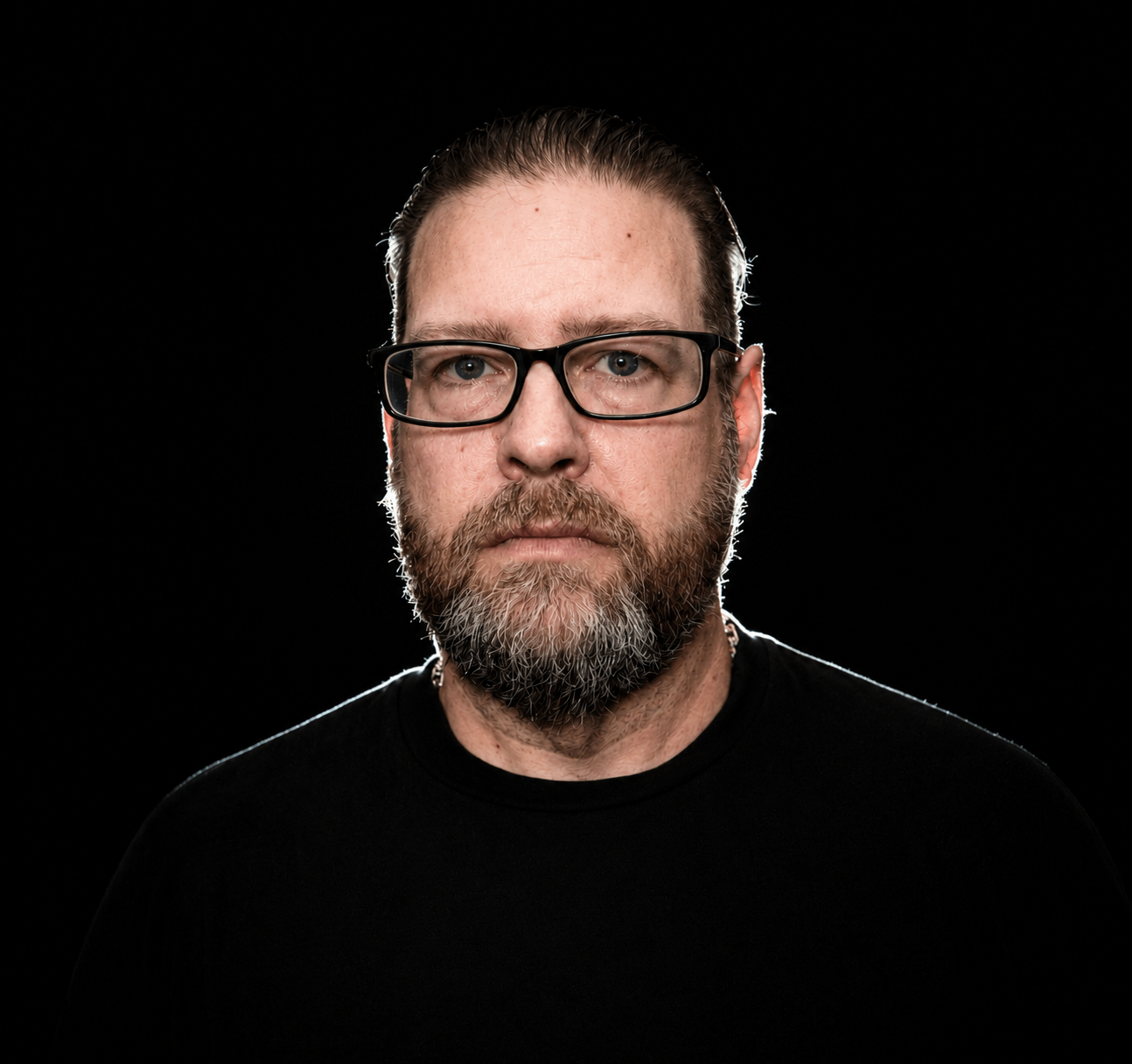 a man with glasses and a beard standing in front of a black background