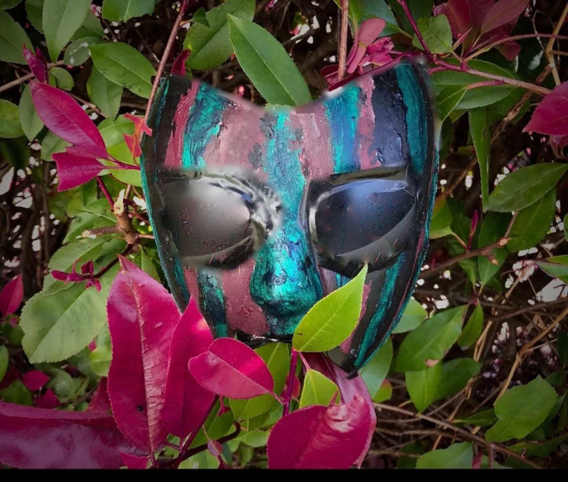 a mask is sitting in a bush with leaves around it