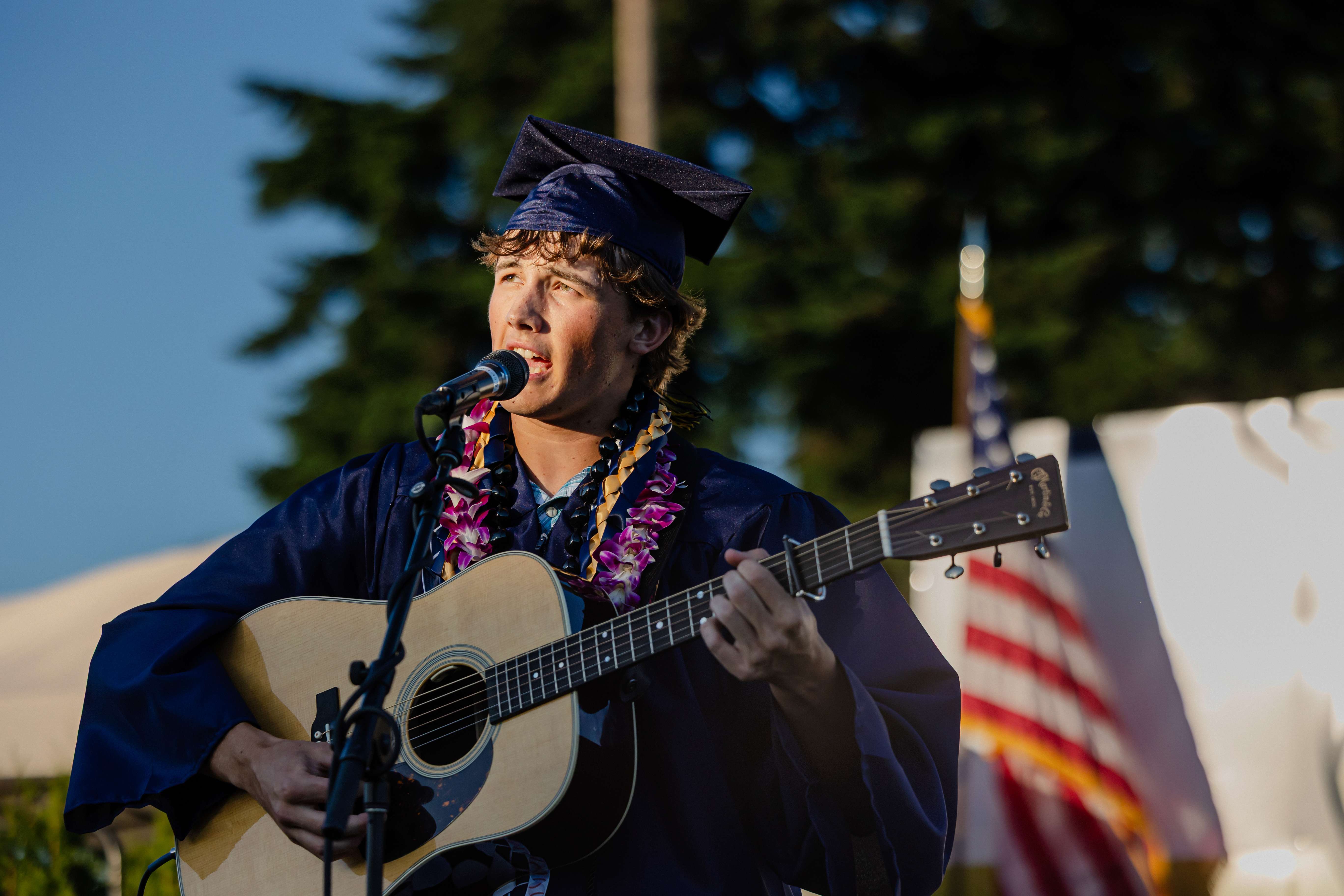a man in a graduation gown singing an acoustic guitar