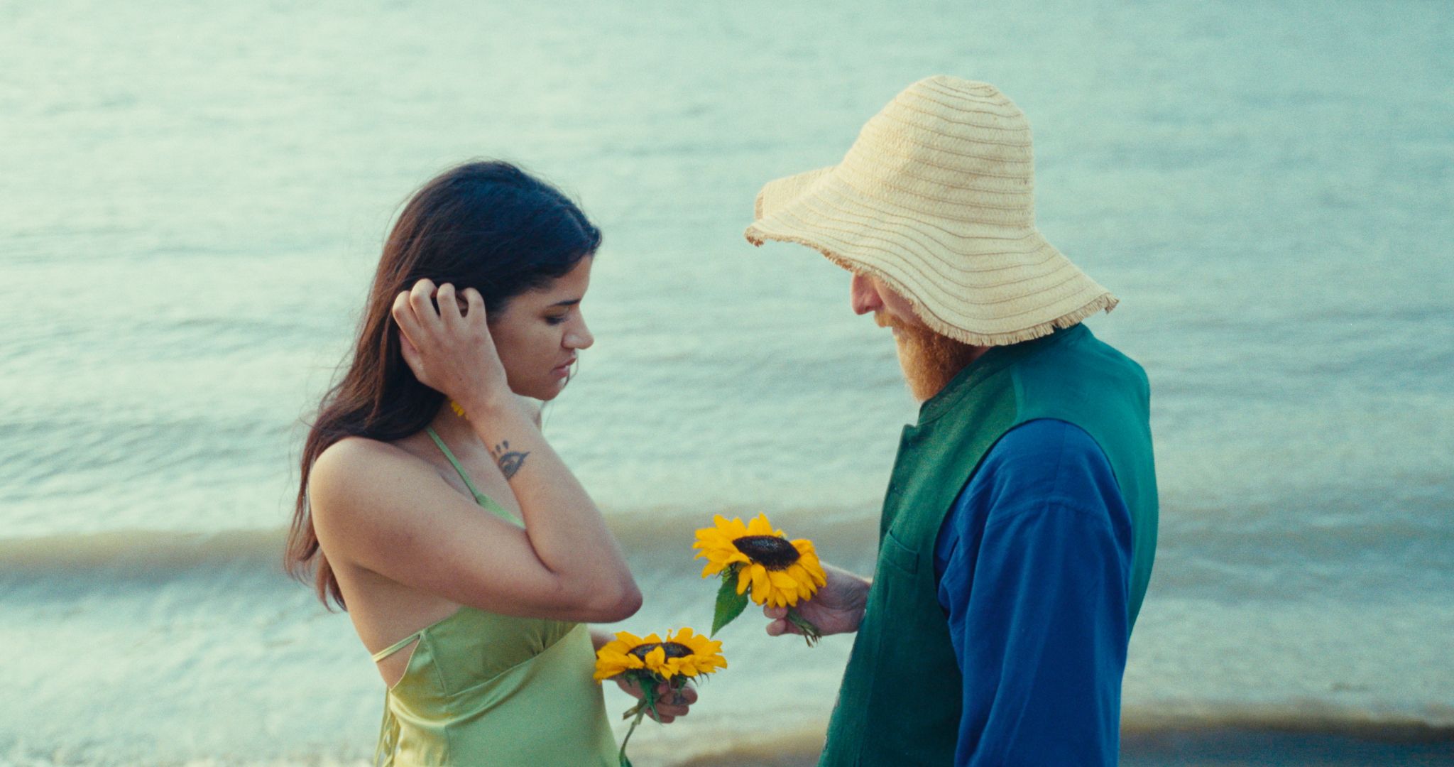 a man and woman holding sunflowers on the beach
