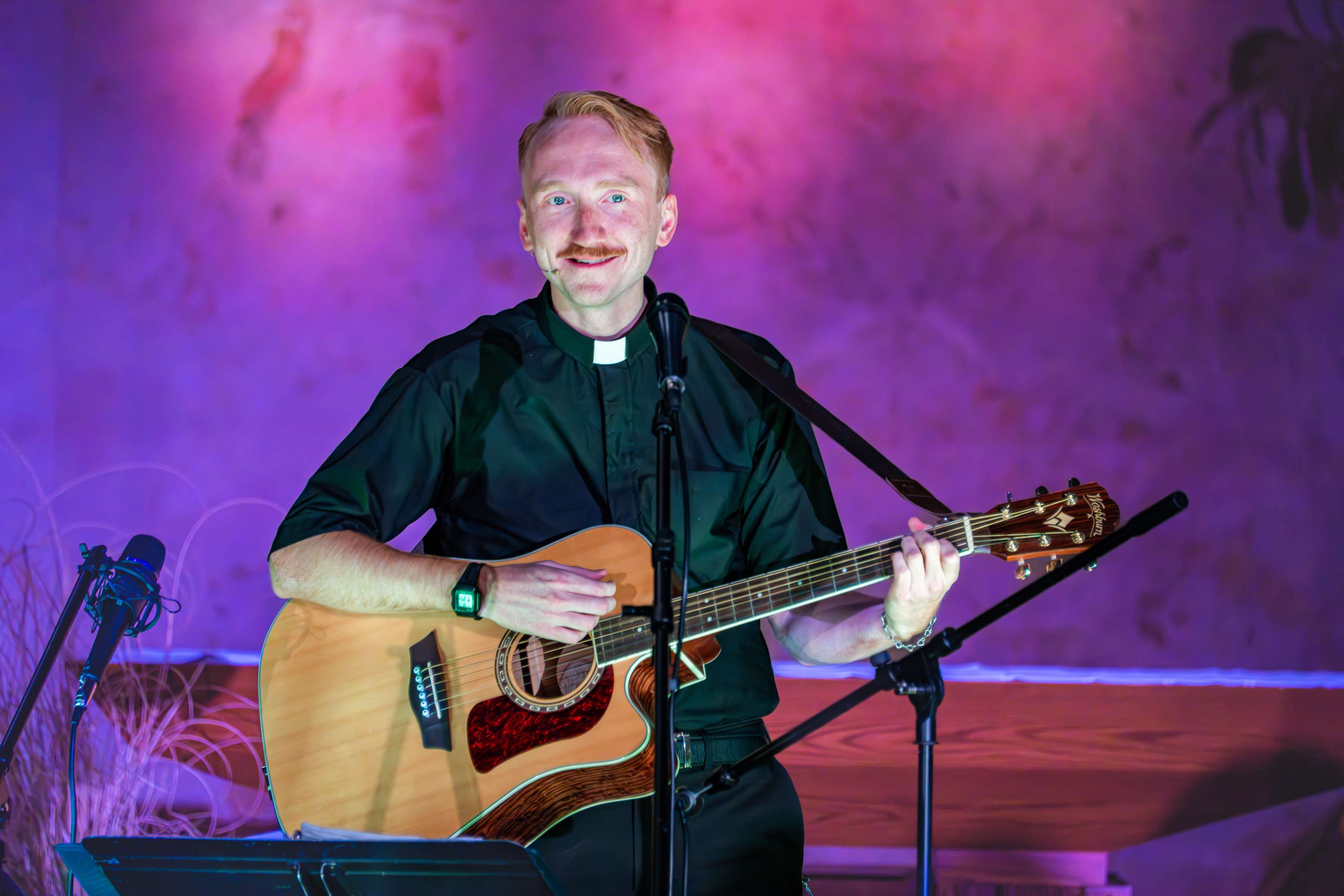 a priest playing an acoustic guitar in front of a microphone