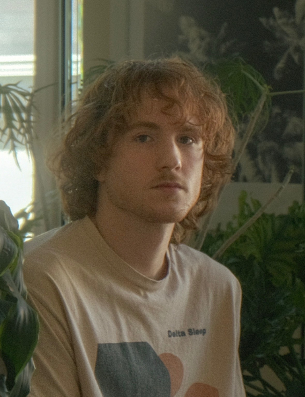 a young man in a t - shirt sitting next to a plant