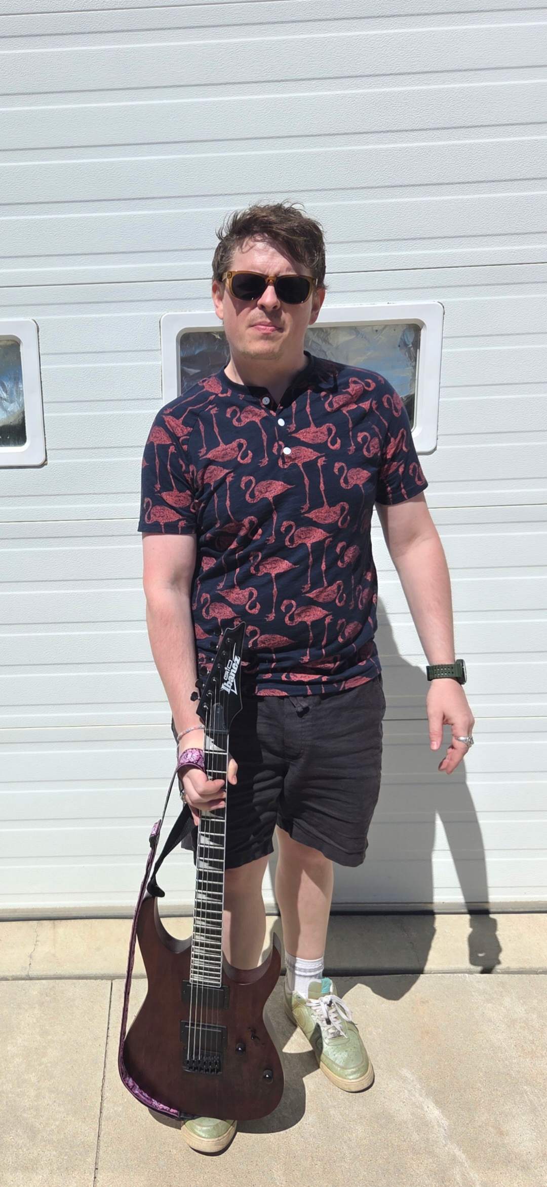 a young man in sunglasses holding a guitar in front of a garage
