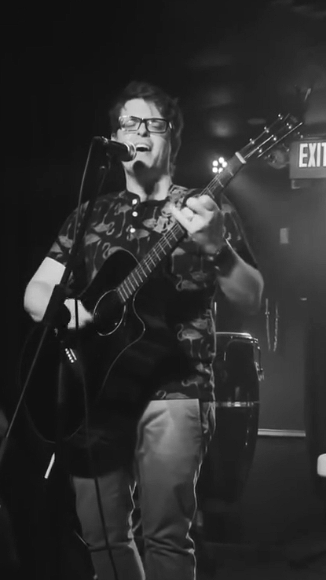 a man in glasses is playing an acoustic guitar in front of a microphone