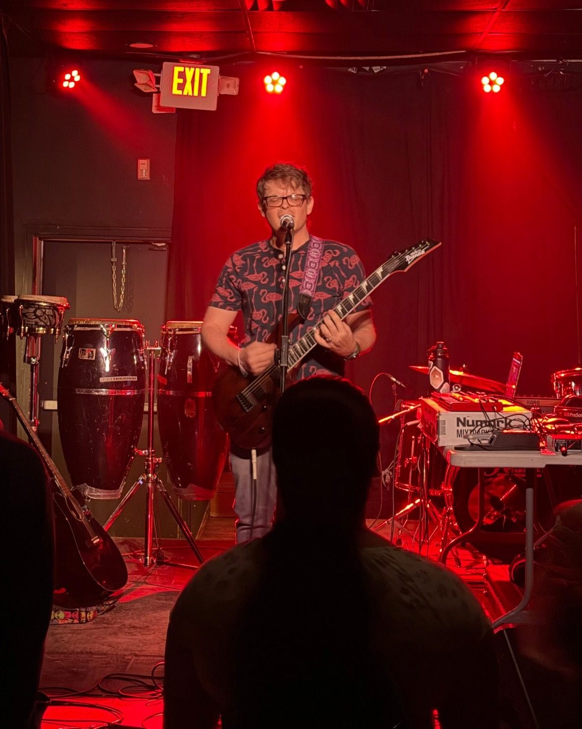 a man playing guitar on stage in front of a red light