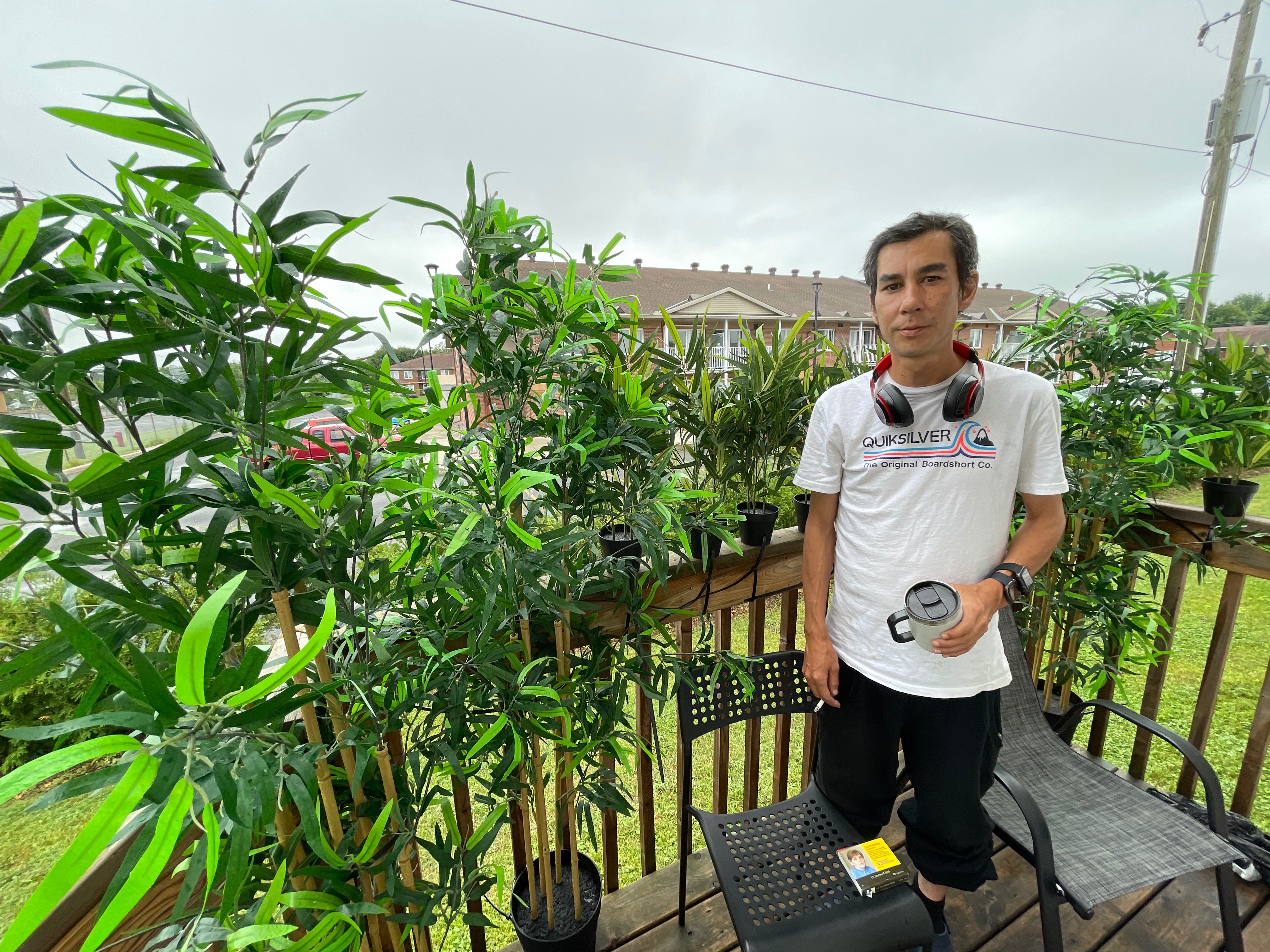 a young man standing next to a potted plant on a deck