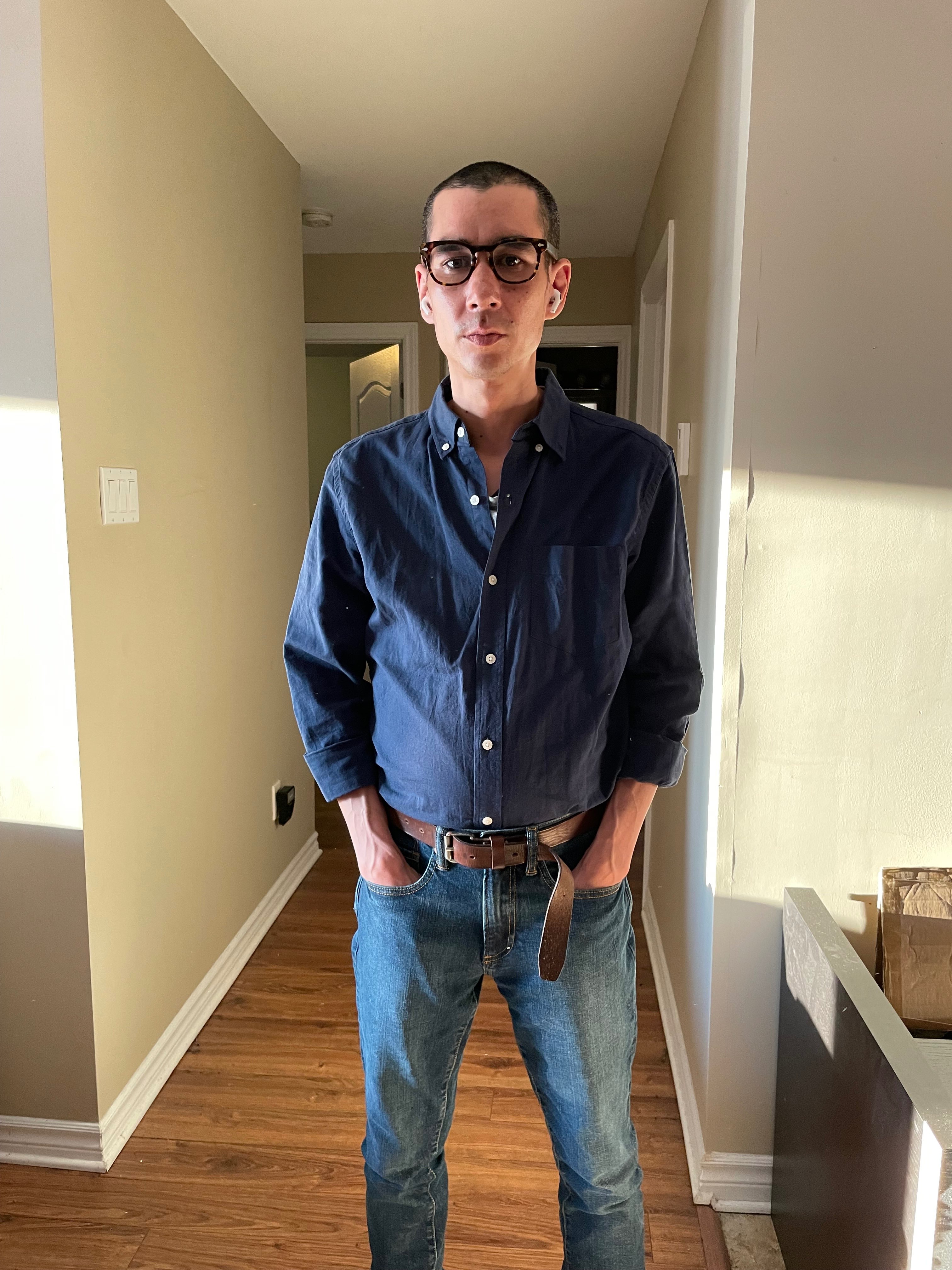 a man wearing glasses and jeans standing in a hallway