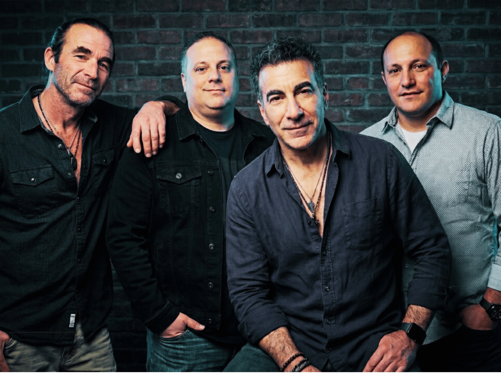 four men posing for a picture in front of a brick wall