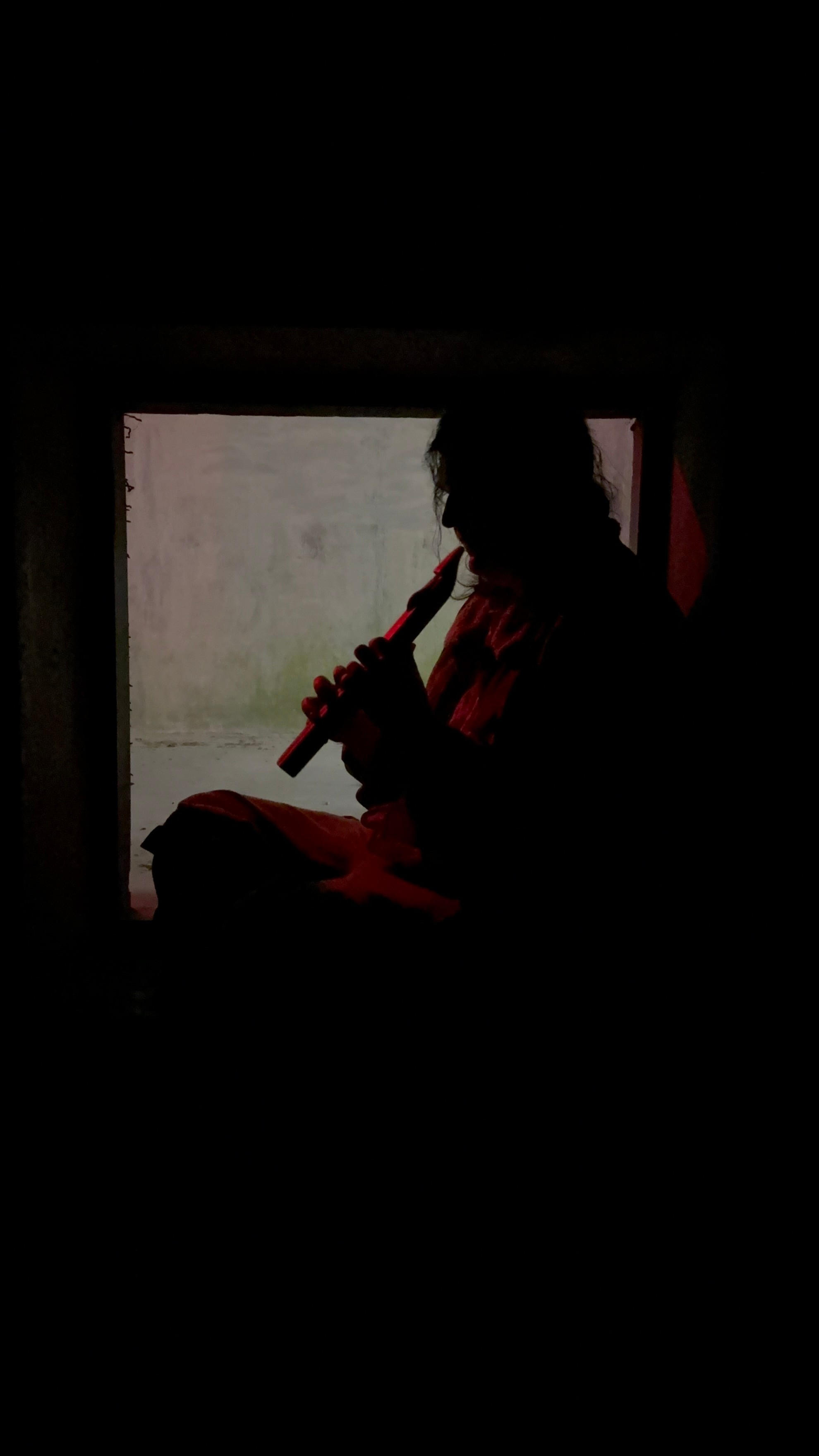 a man playing a flute in front of a window