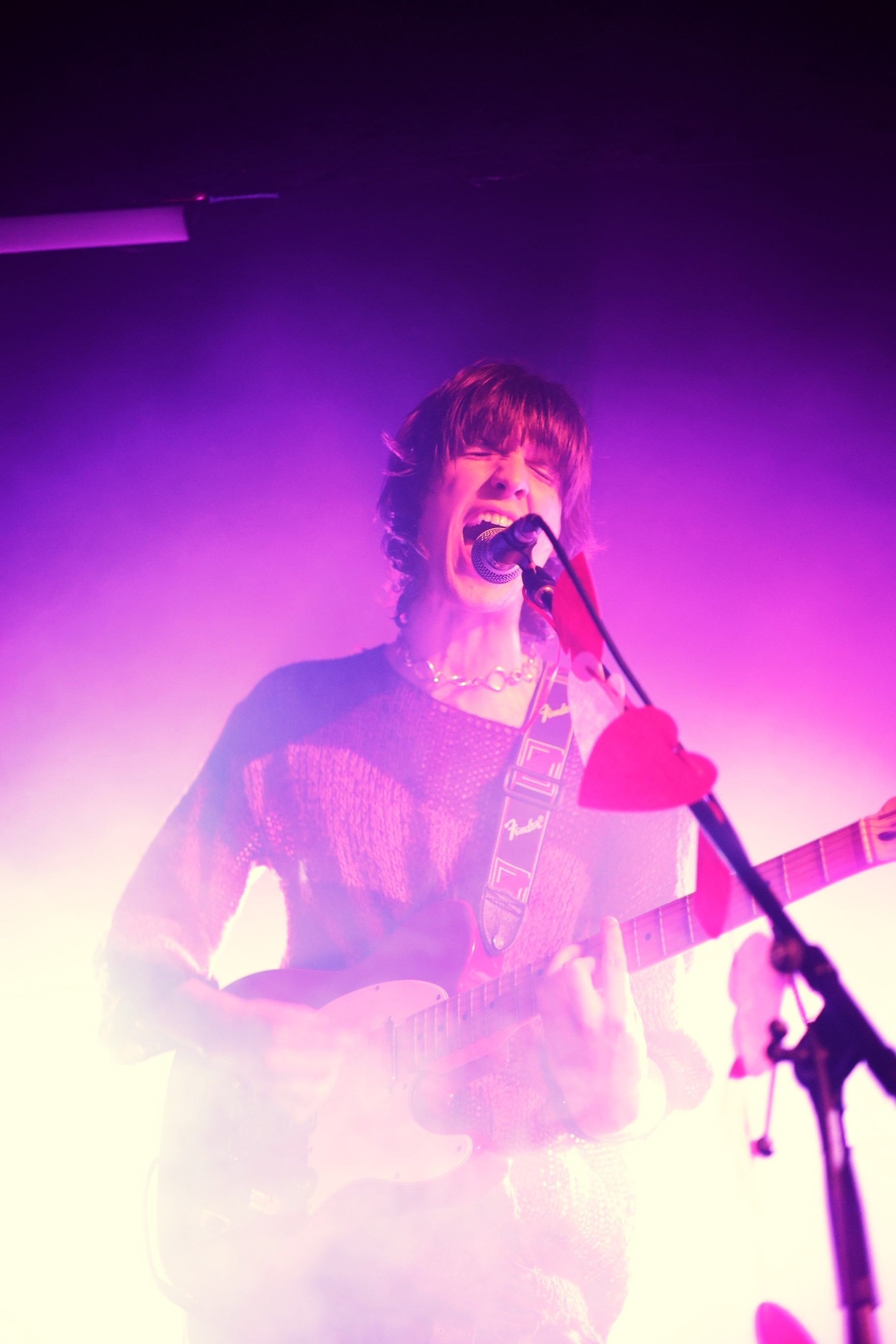 a man playing a guitar in front of a purple light