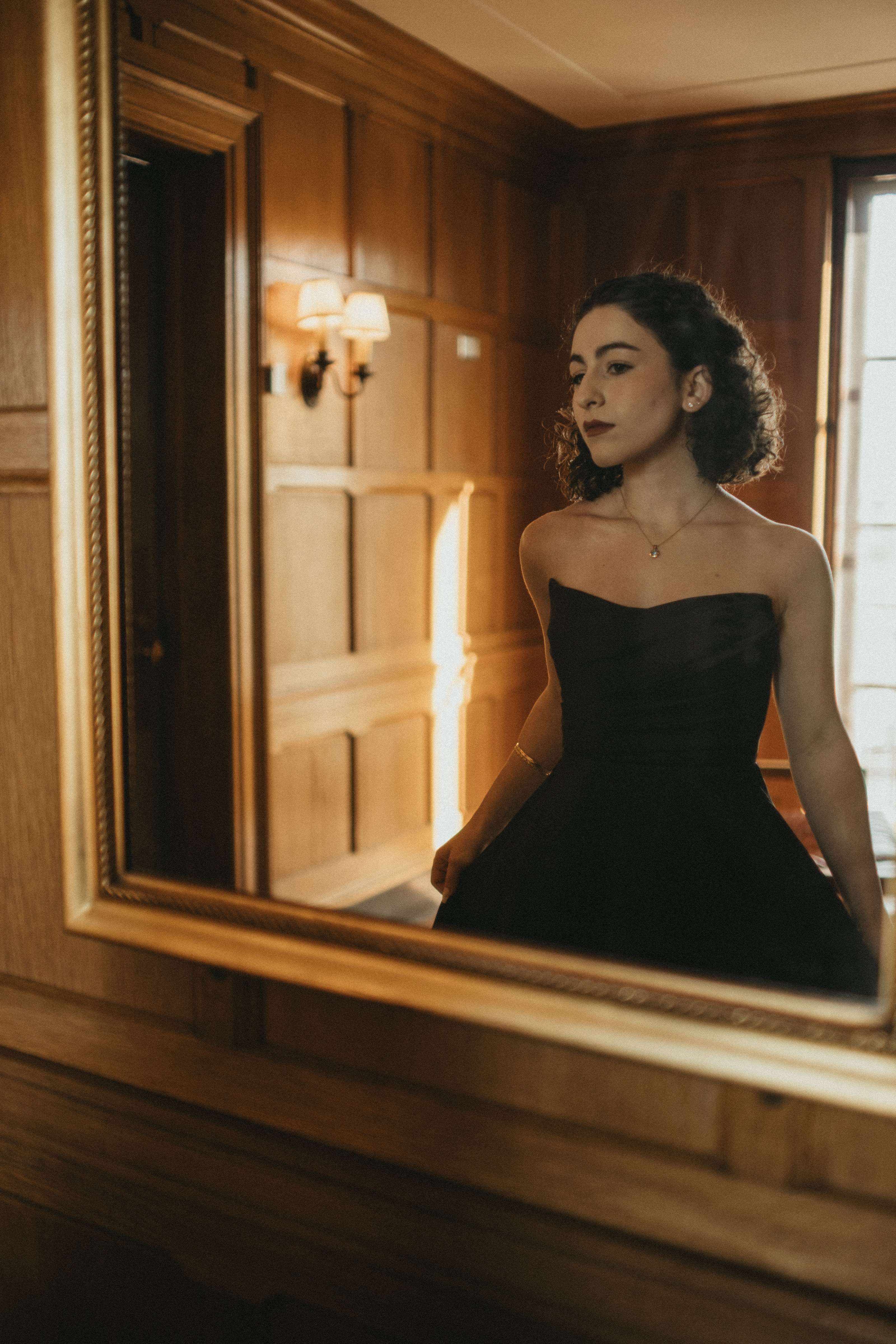 a woman in a black dress is standing in front of a mirror