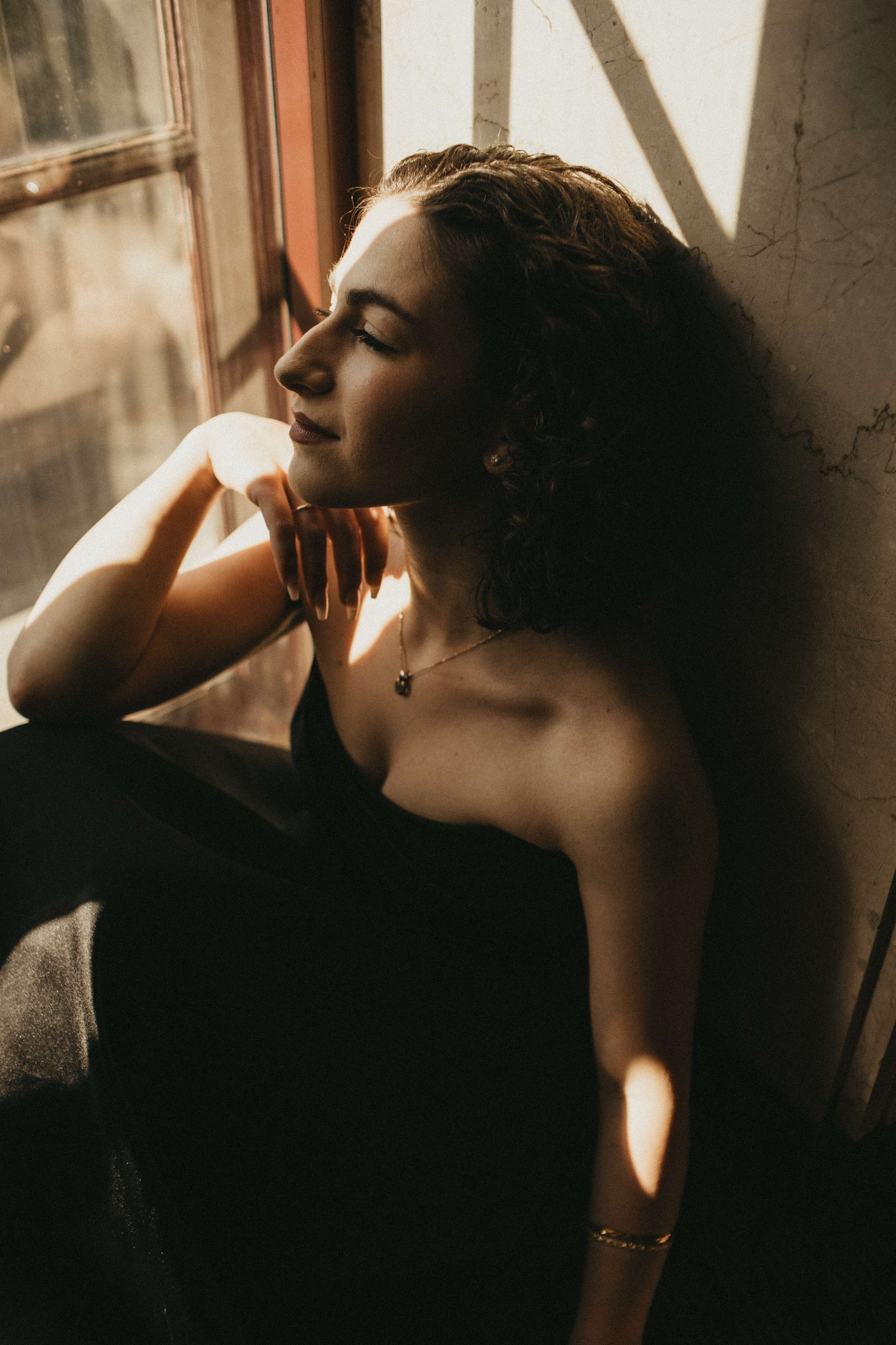 a woman in a black dress leaning against a window