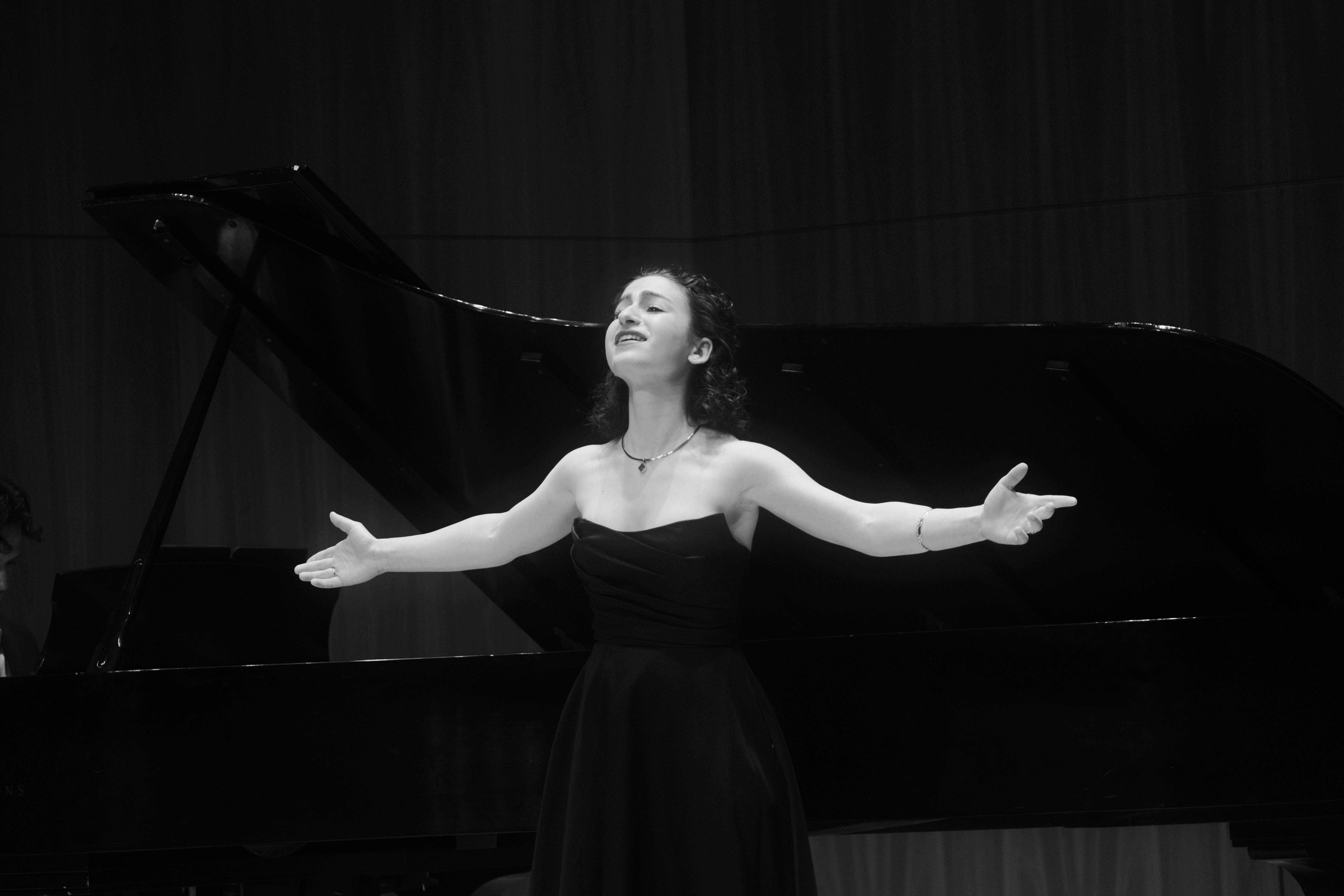 a woman in a black dress with her arms outstretched in front of a piano