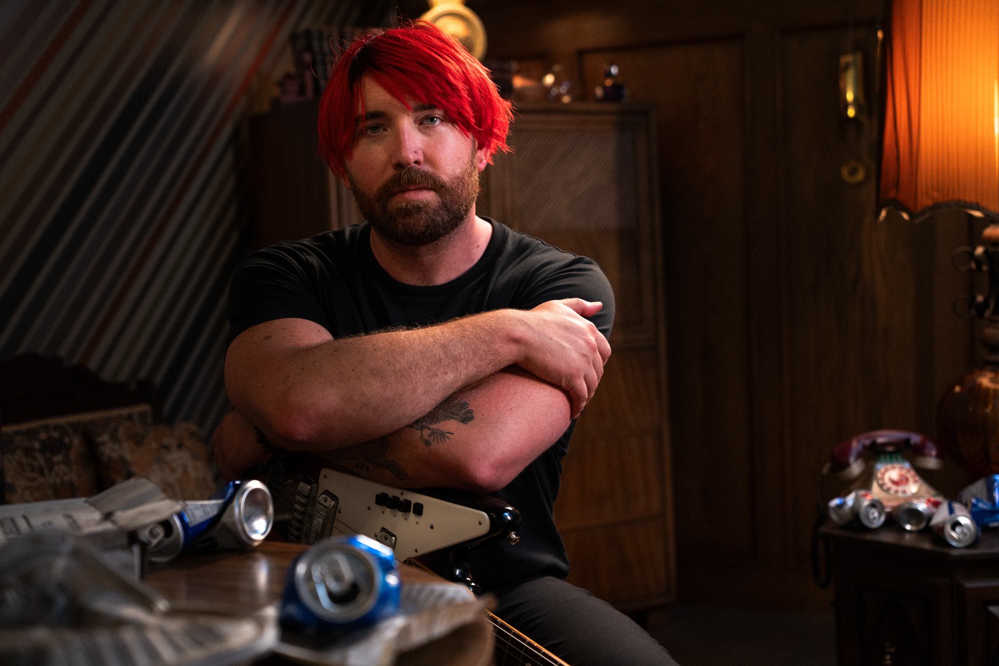 a man with red hair sitting in front of a room full of cans