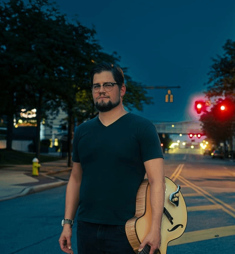 a man with a guitar standing on a street at night
