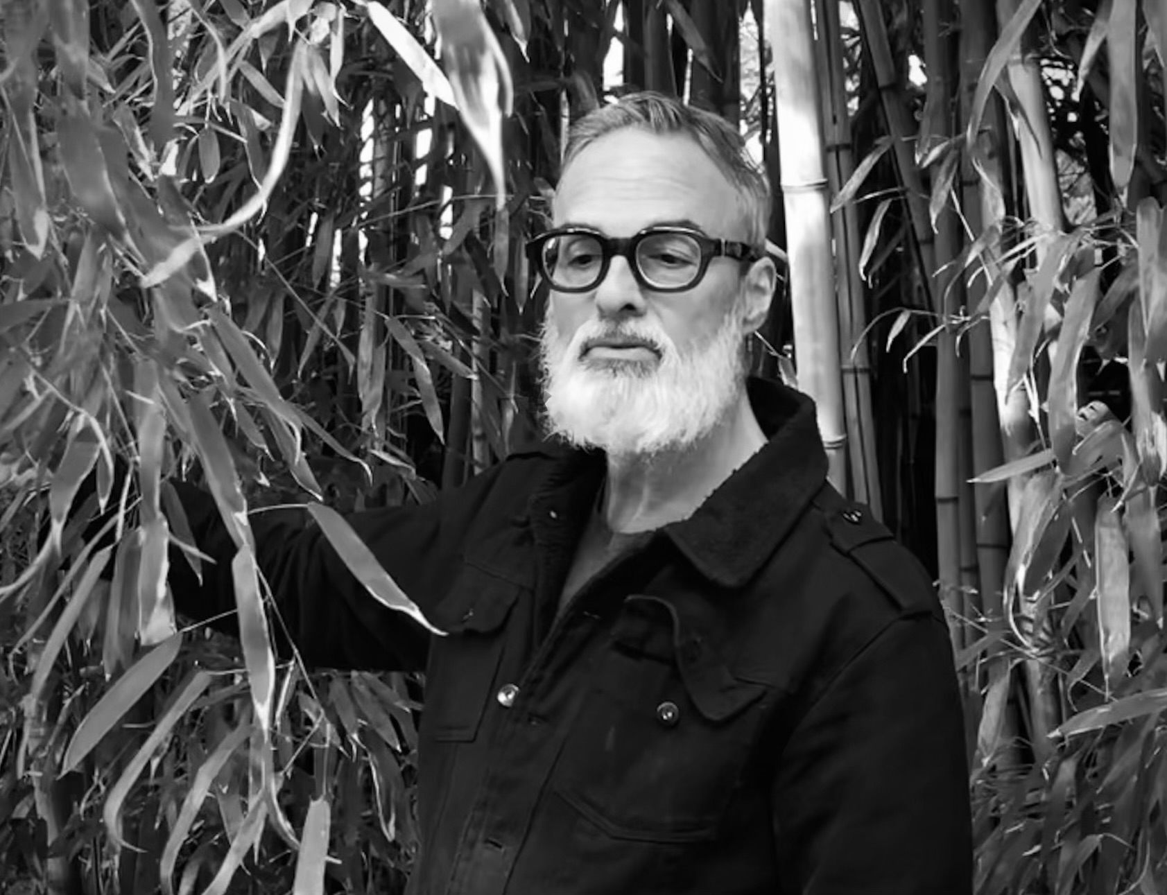 a man with a beard standing in front of bamboo plants