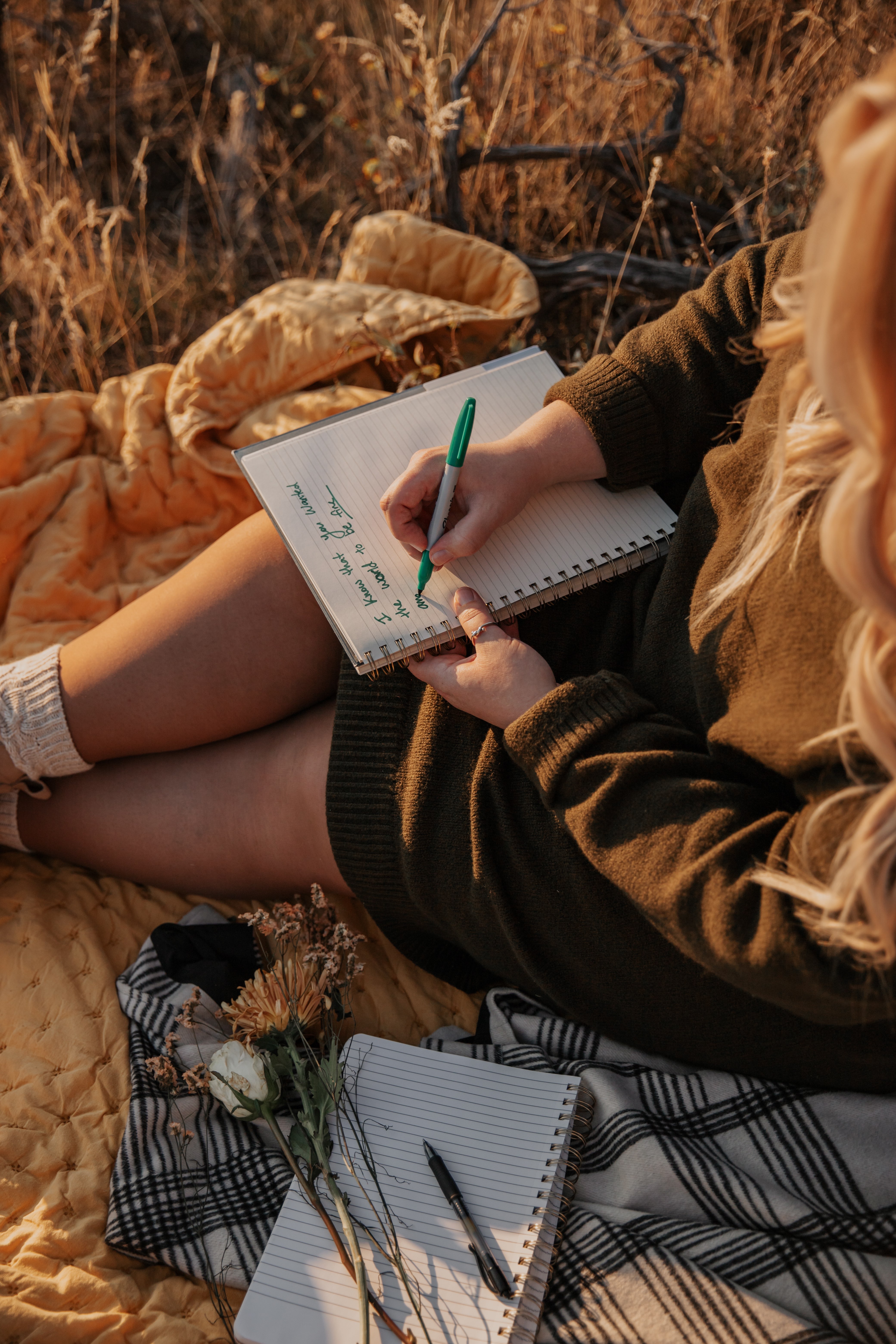 a woman sits on a blanket and writes in a notebook