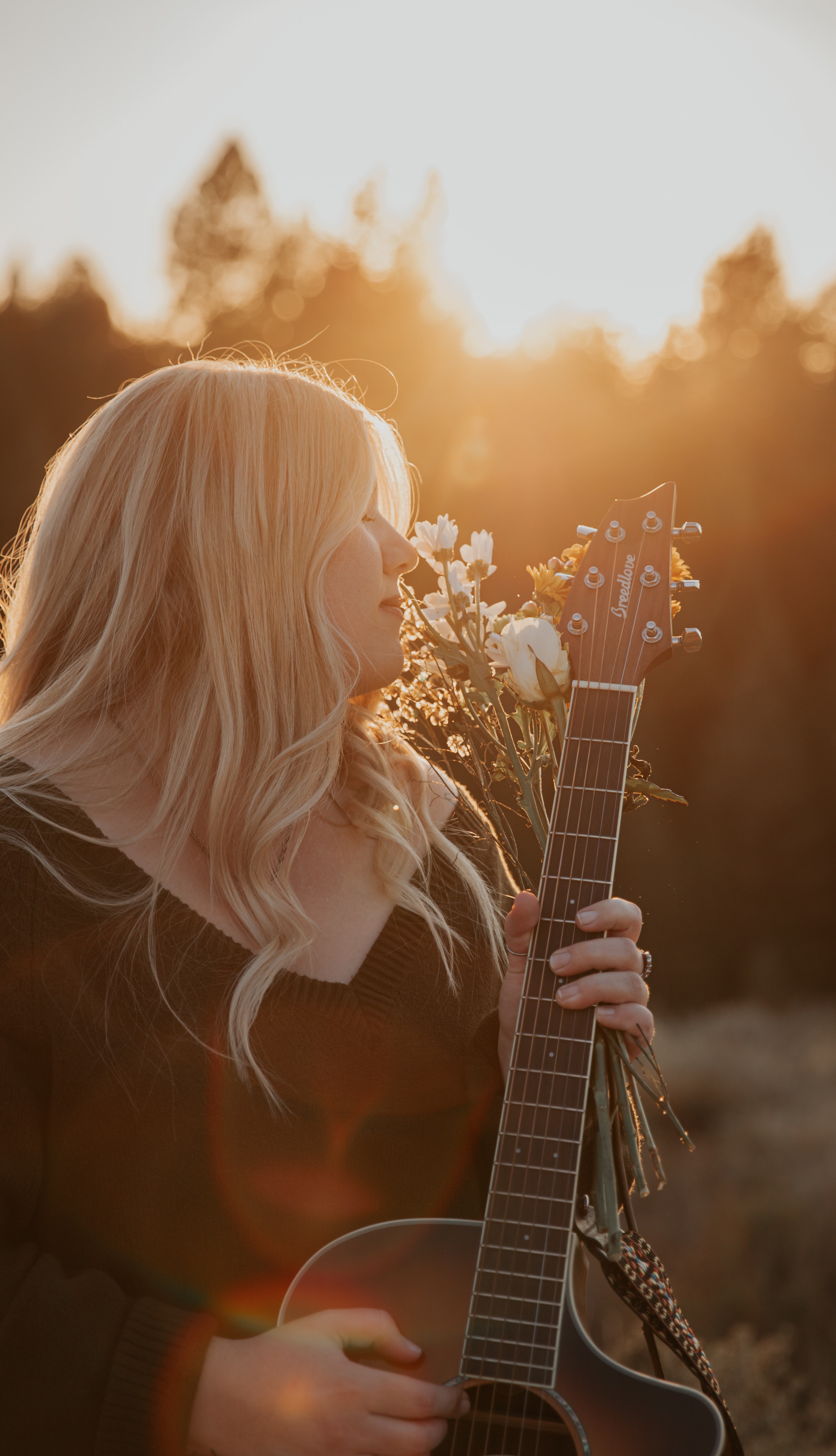 a woman holding an acoustic guitar at sunset