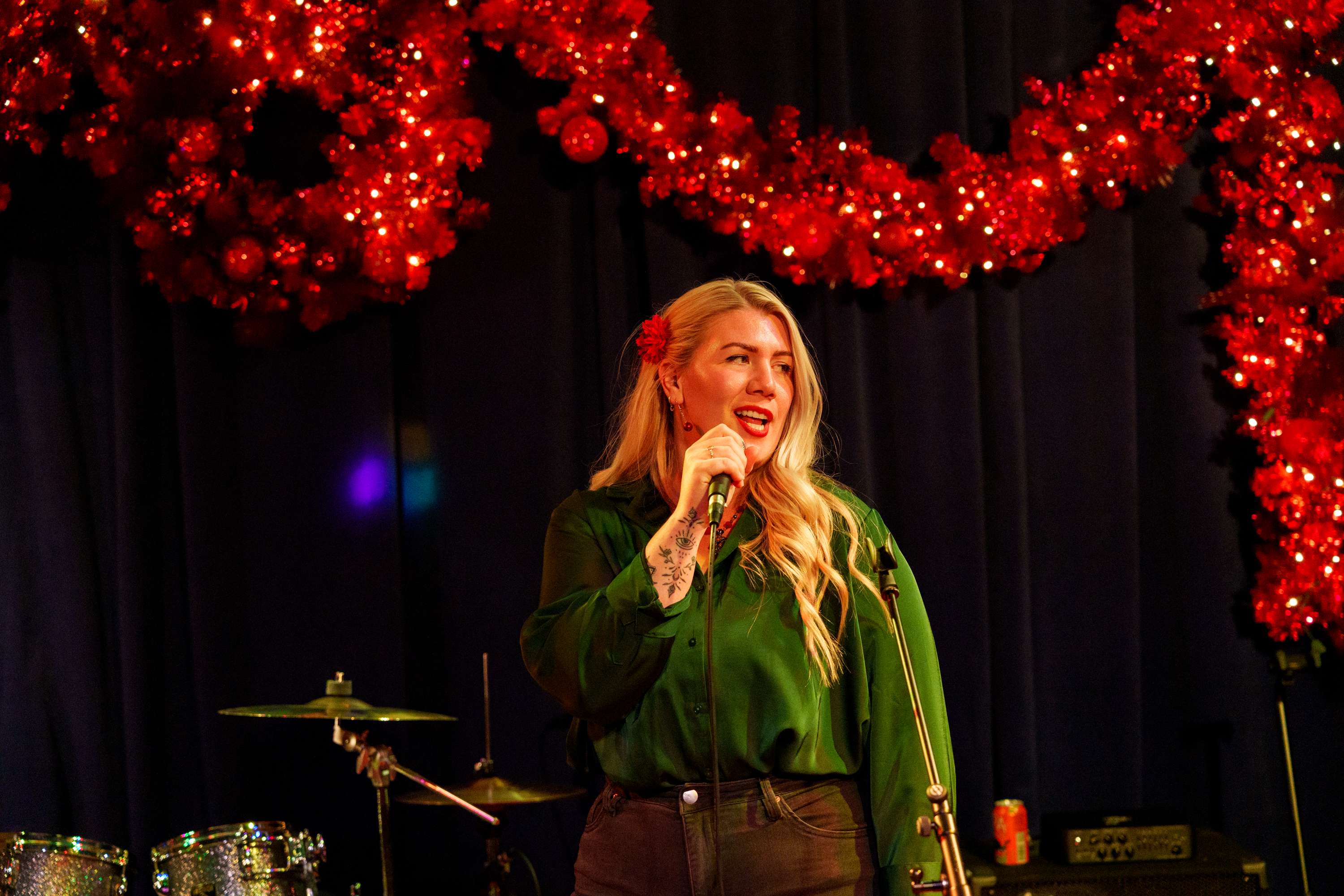 a woman singing into a microphone in front of a christmas tree