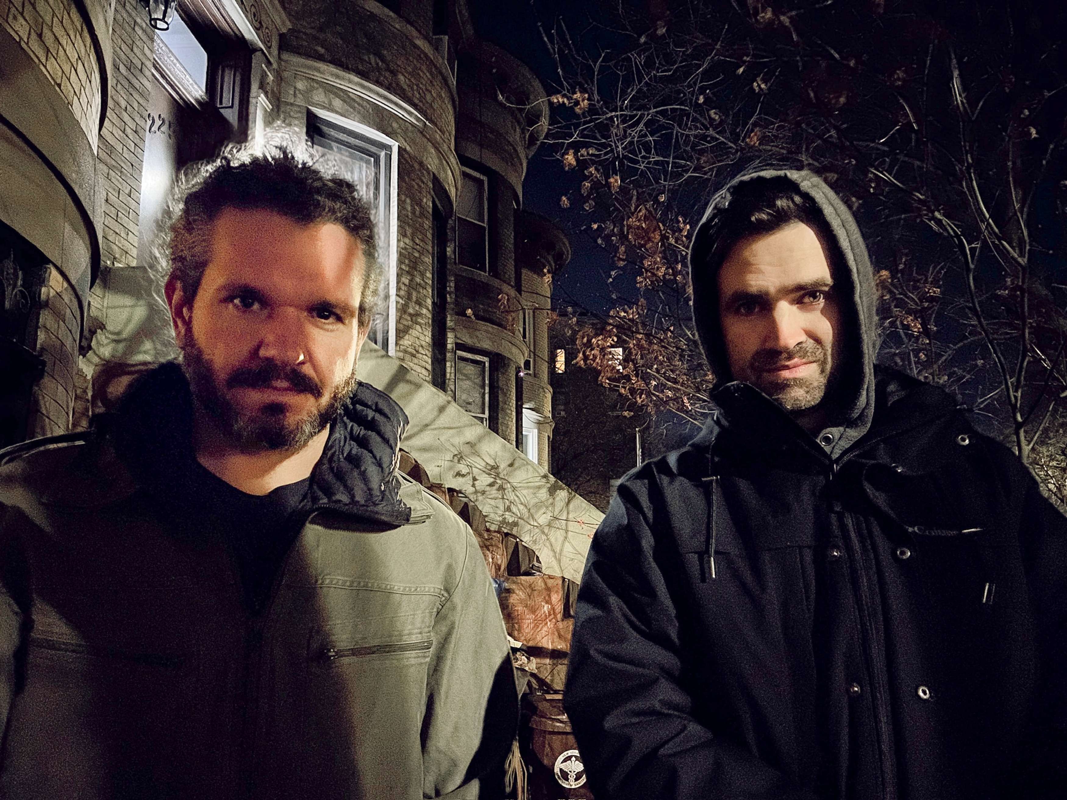 two men standing in front of a house at night