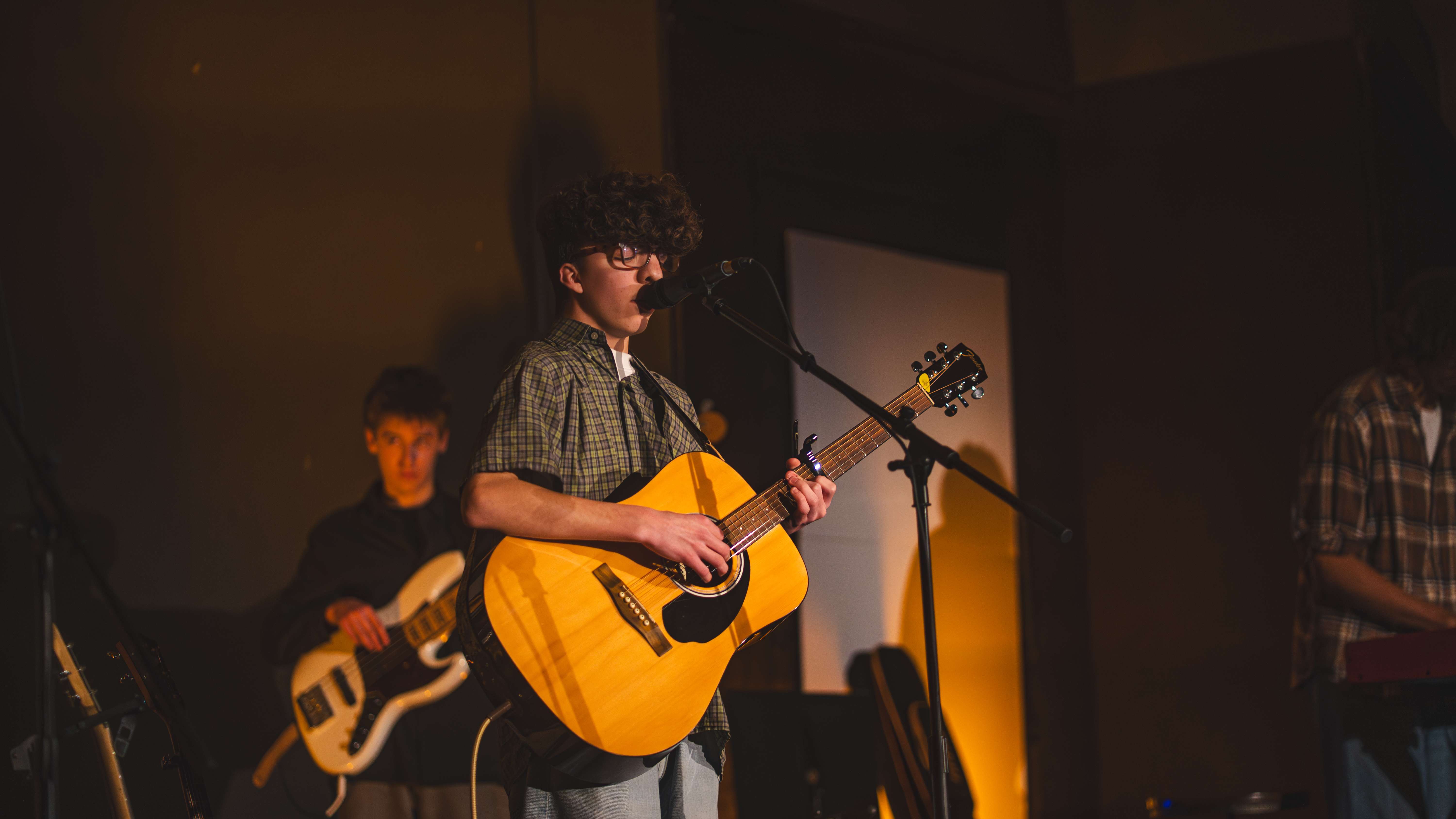 a young man playing an acoustic guitar in front of a microphone