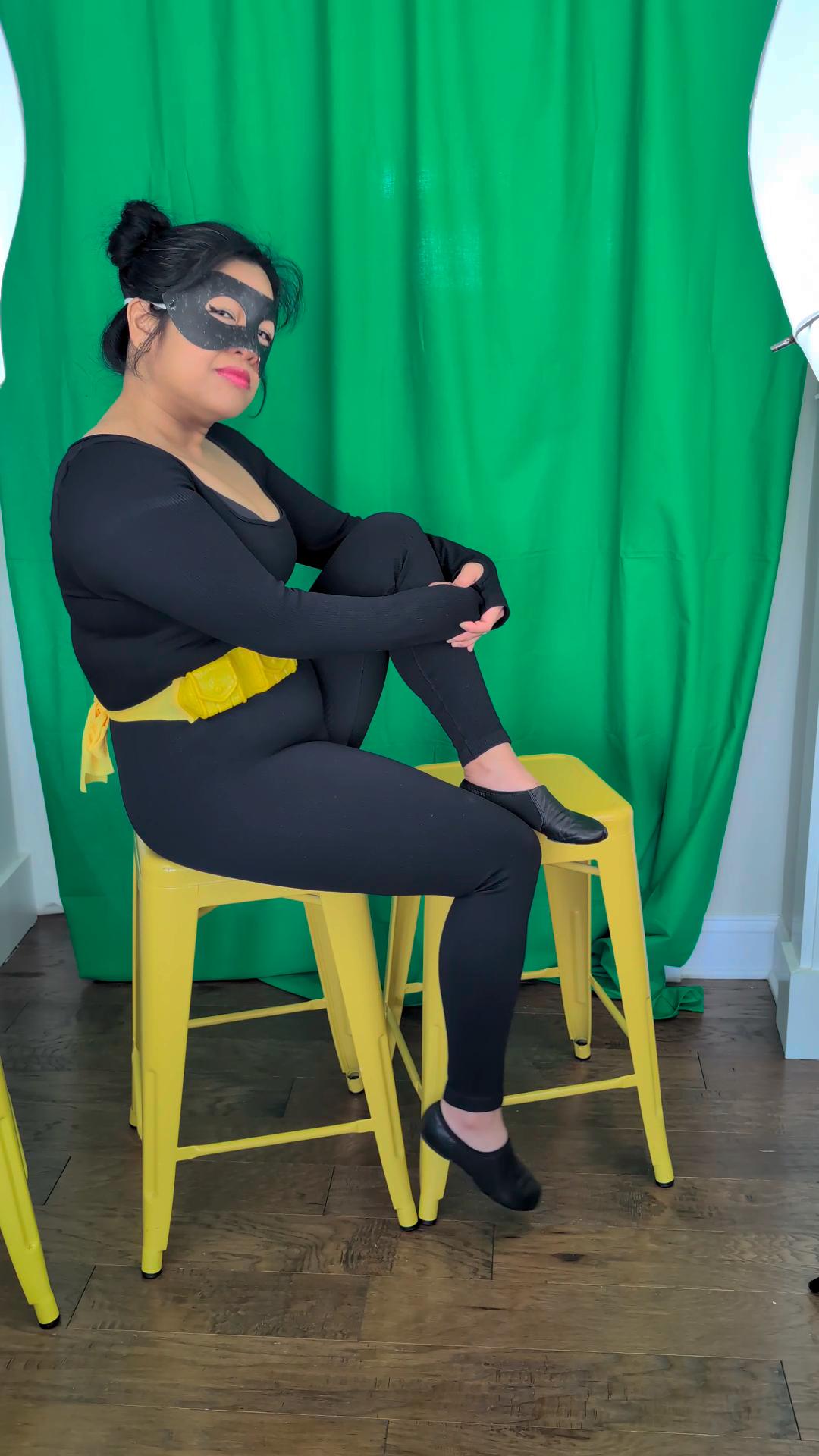 a woman dressed as a batman sits on a stool