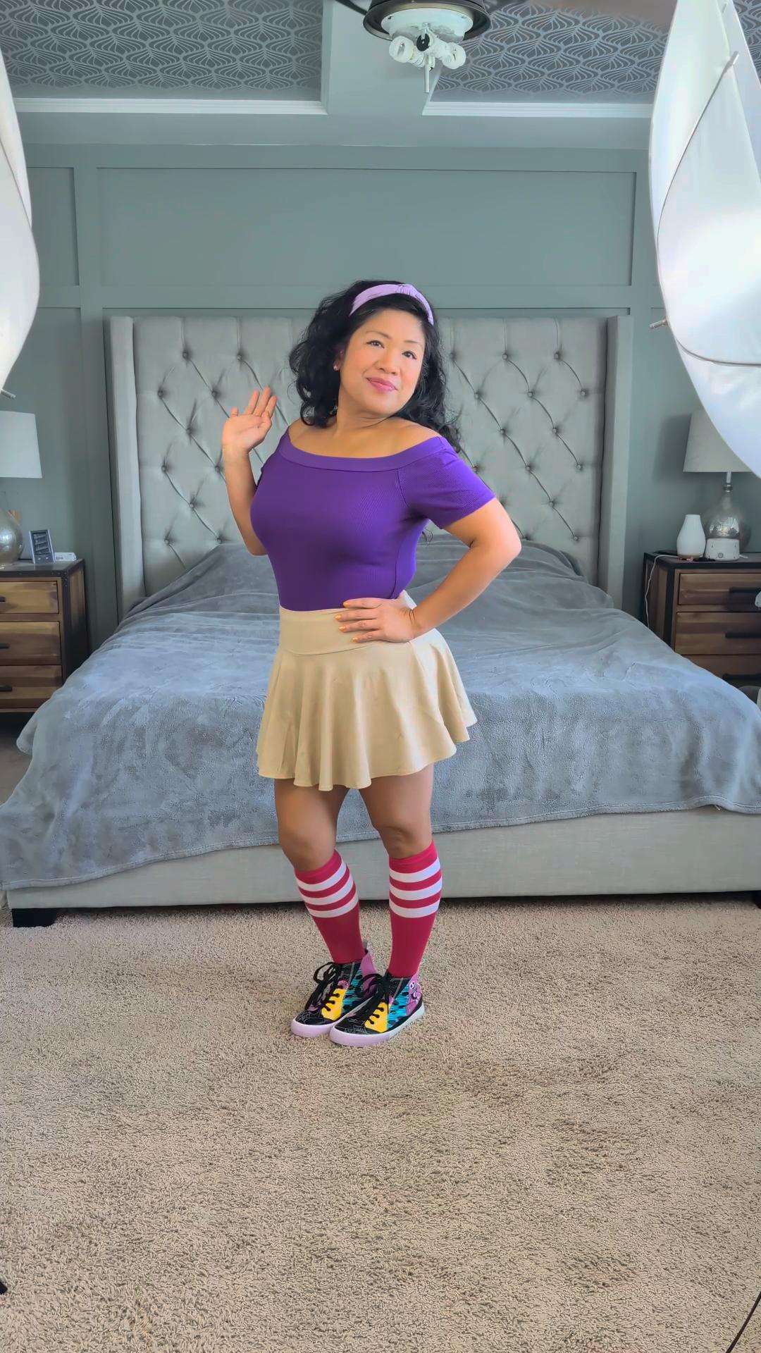a woman in a purple skirt posing in front of a bed