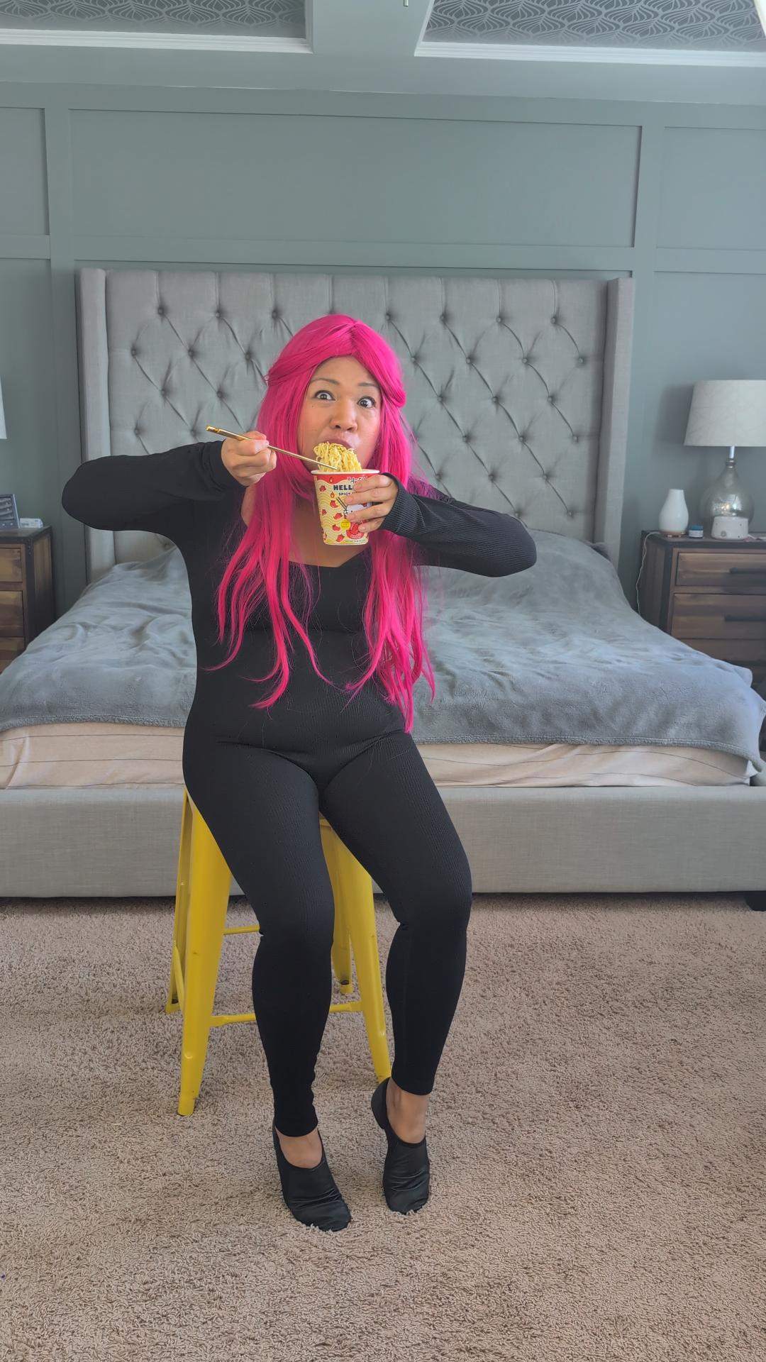 a woman with pink hair sitting on a yellow stool eating a pizza