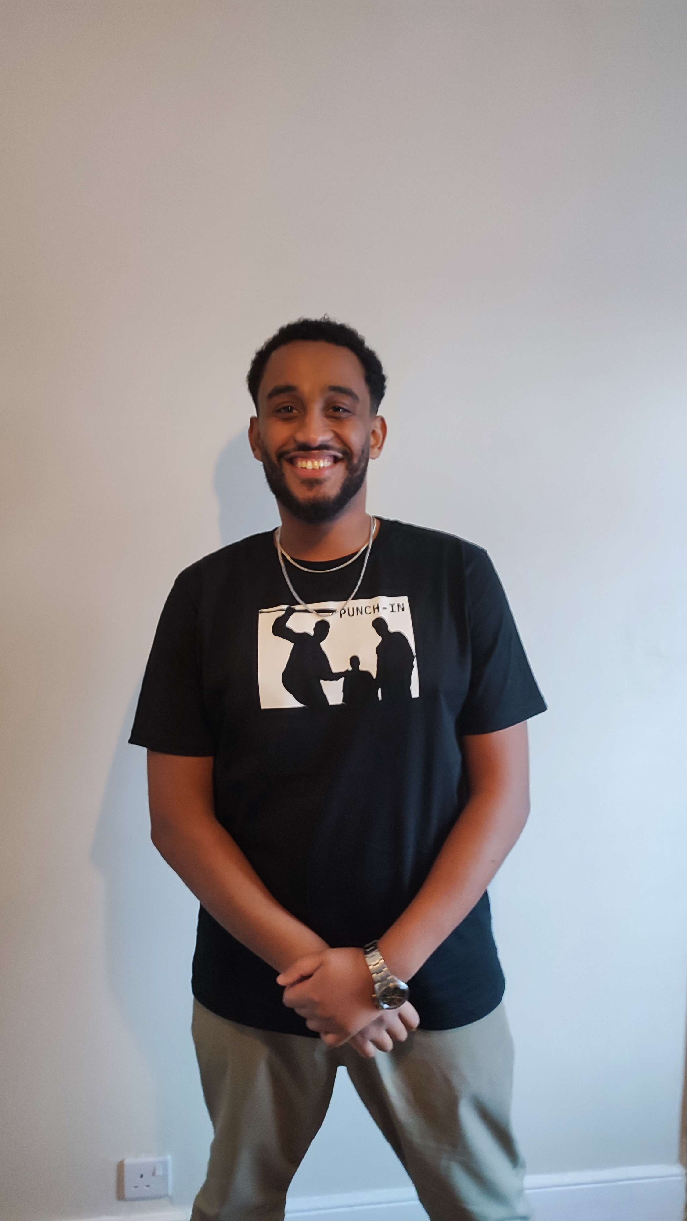 a young man wearing a black t - shirt standing in front of a white wall