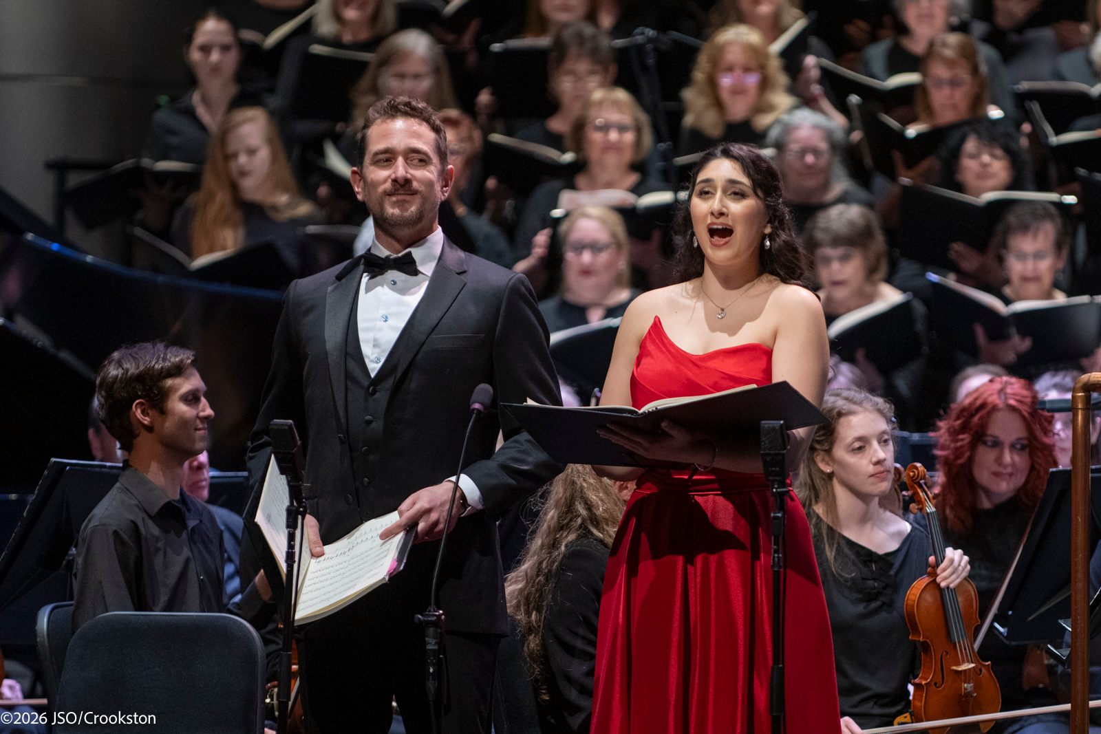 a man and woman singing in front of an orchestra