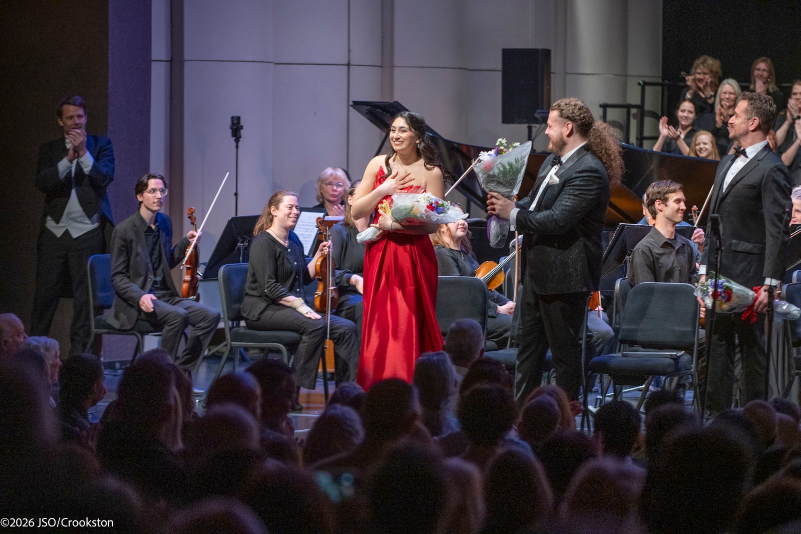 a woman in a red dress is holding a bouquet in front of an orchestra