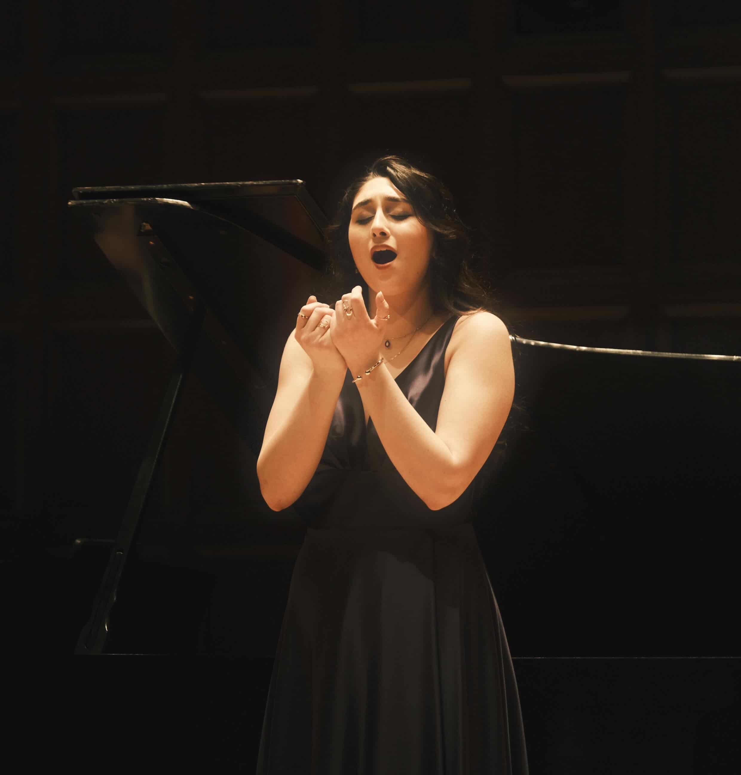 a woman in a black dress singing in front of a piano