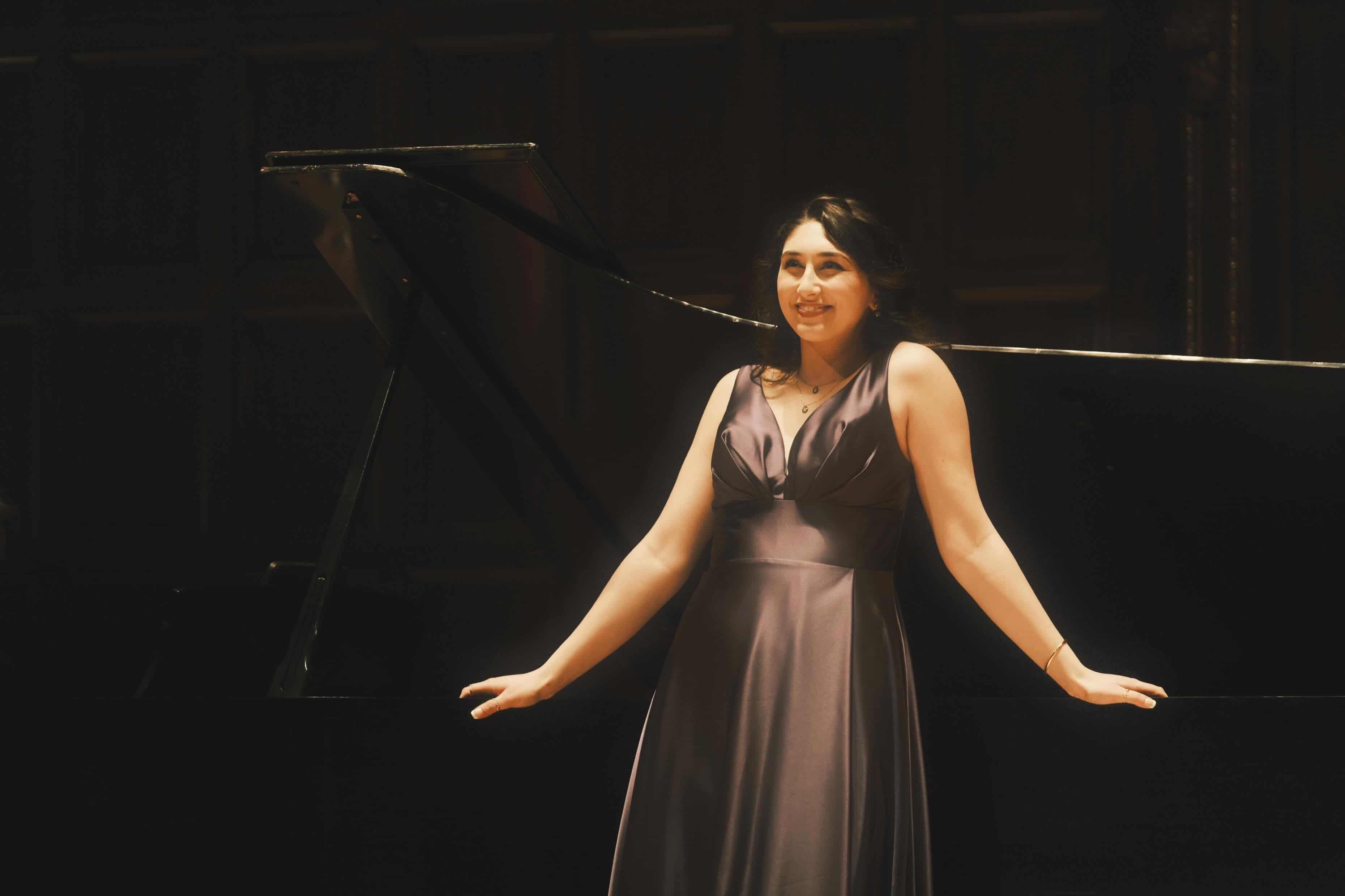 a woman in a long dress standing in front of a piano